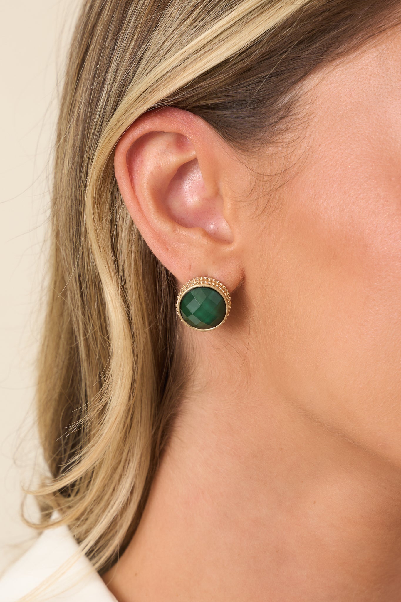 Detailed view of green faceted stud earrings featuring a luminous gemstone center and delicate gold border.