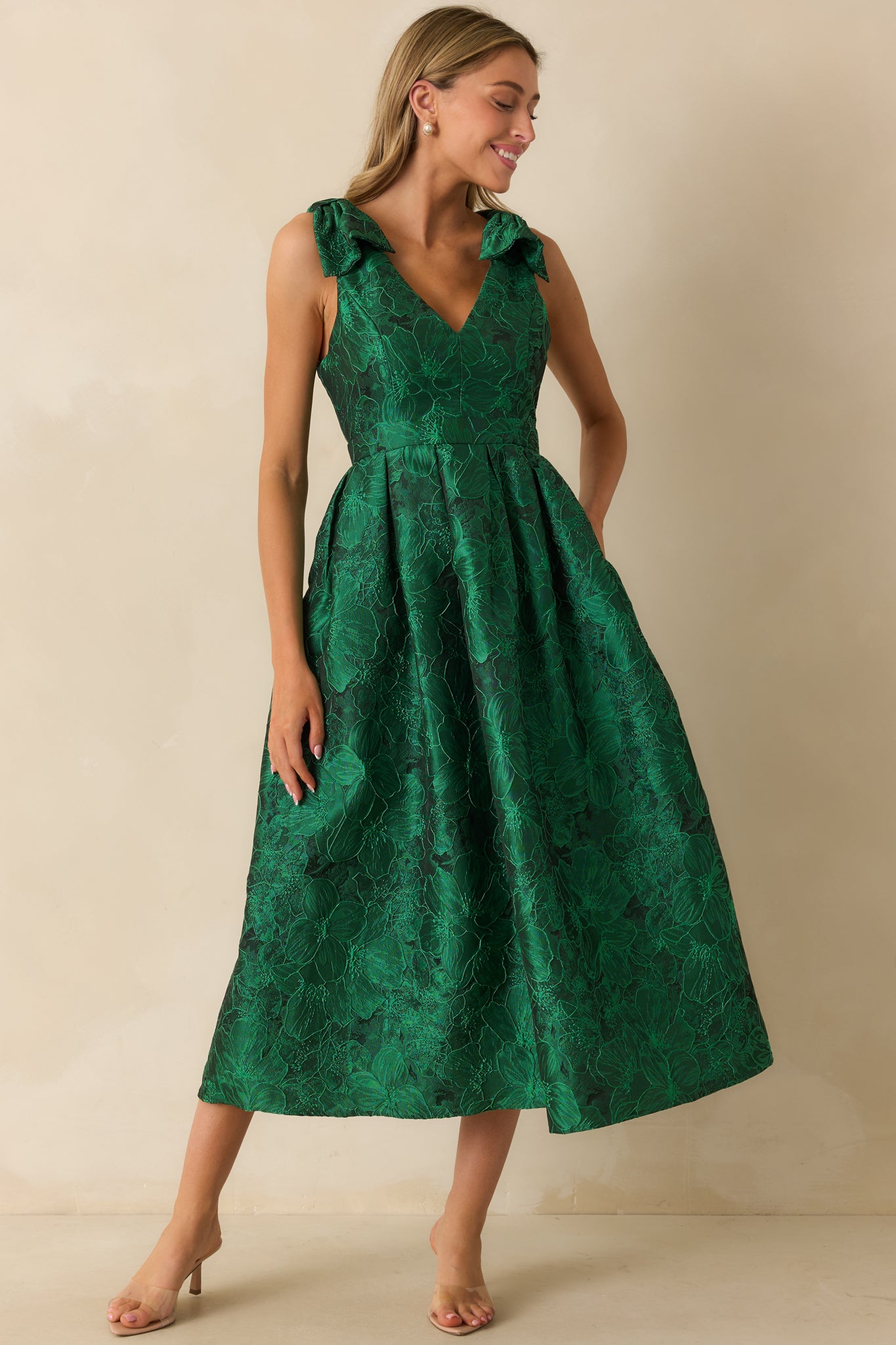Front view of green dress highlighting floral pattern, adjustable bow straps, and flowing mid-length skirt.