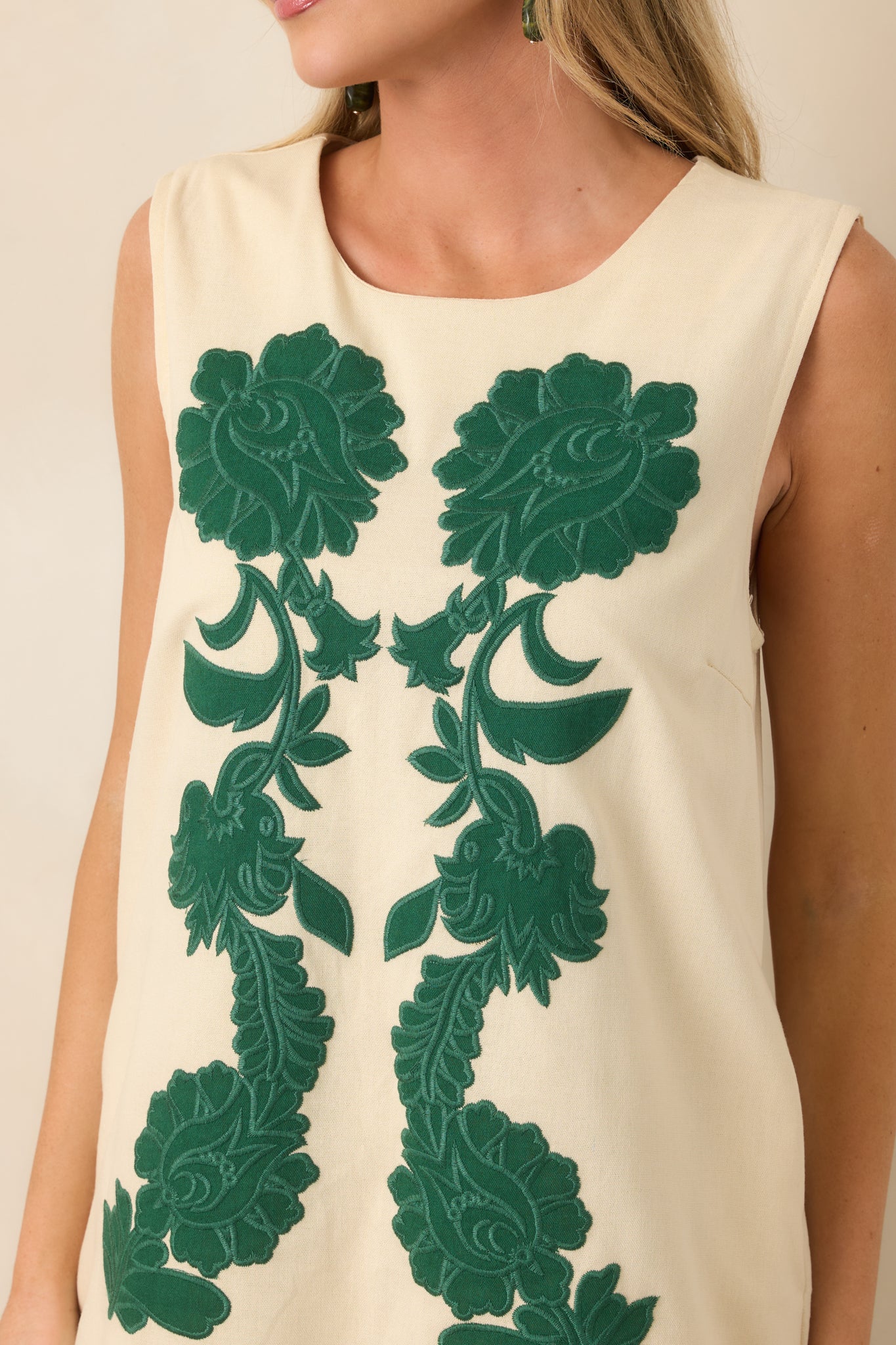 Close-up of the oversized green floral embroidery, highlighting its dimensional texture against the contrasting ivory fabric.