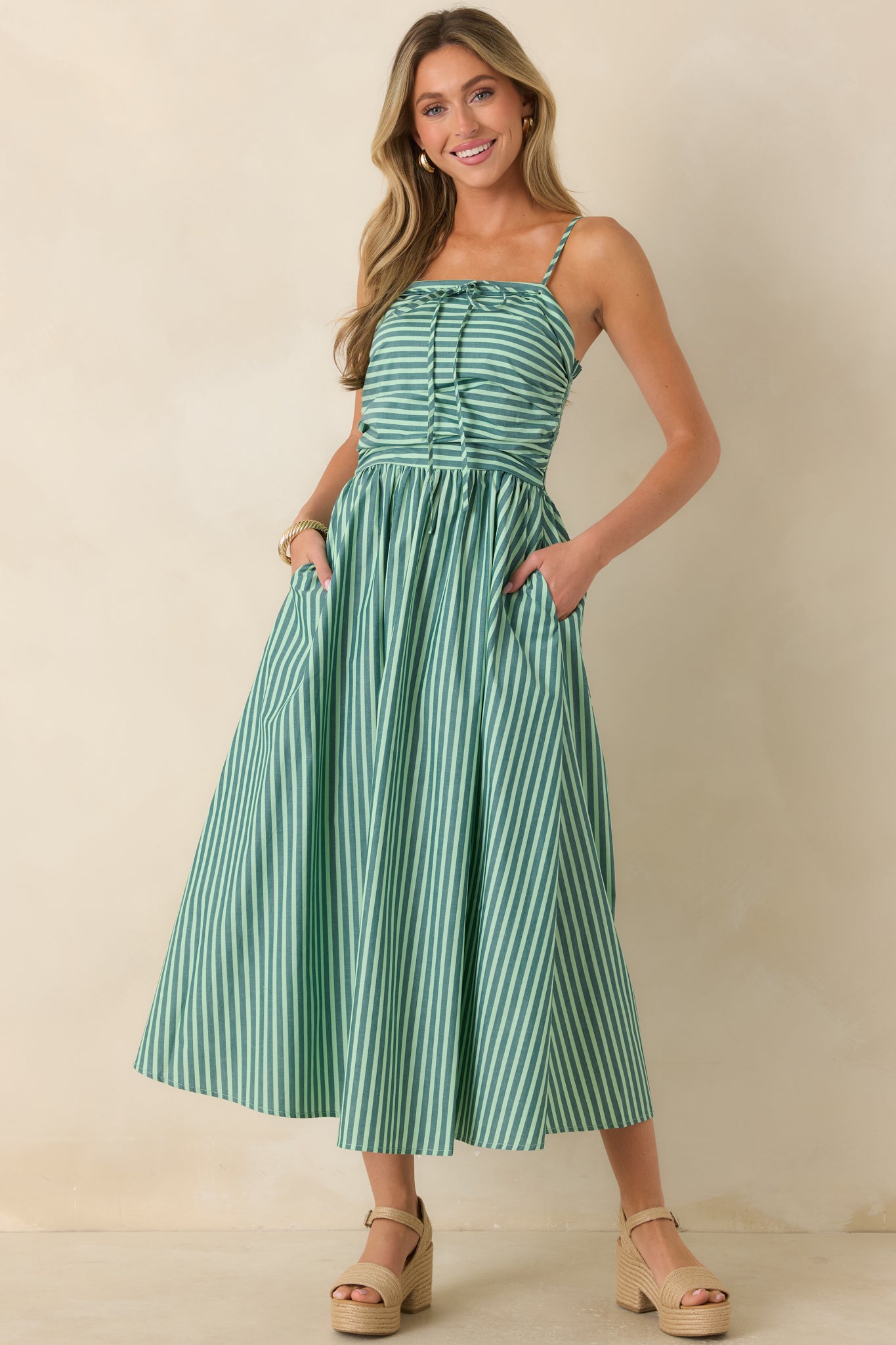 Green and ivory striped cotton maxi dress featuring a softly ruched bodice, straight neckline, adjustable shoulder straps, and a flowing full-length skirt with side pockets.