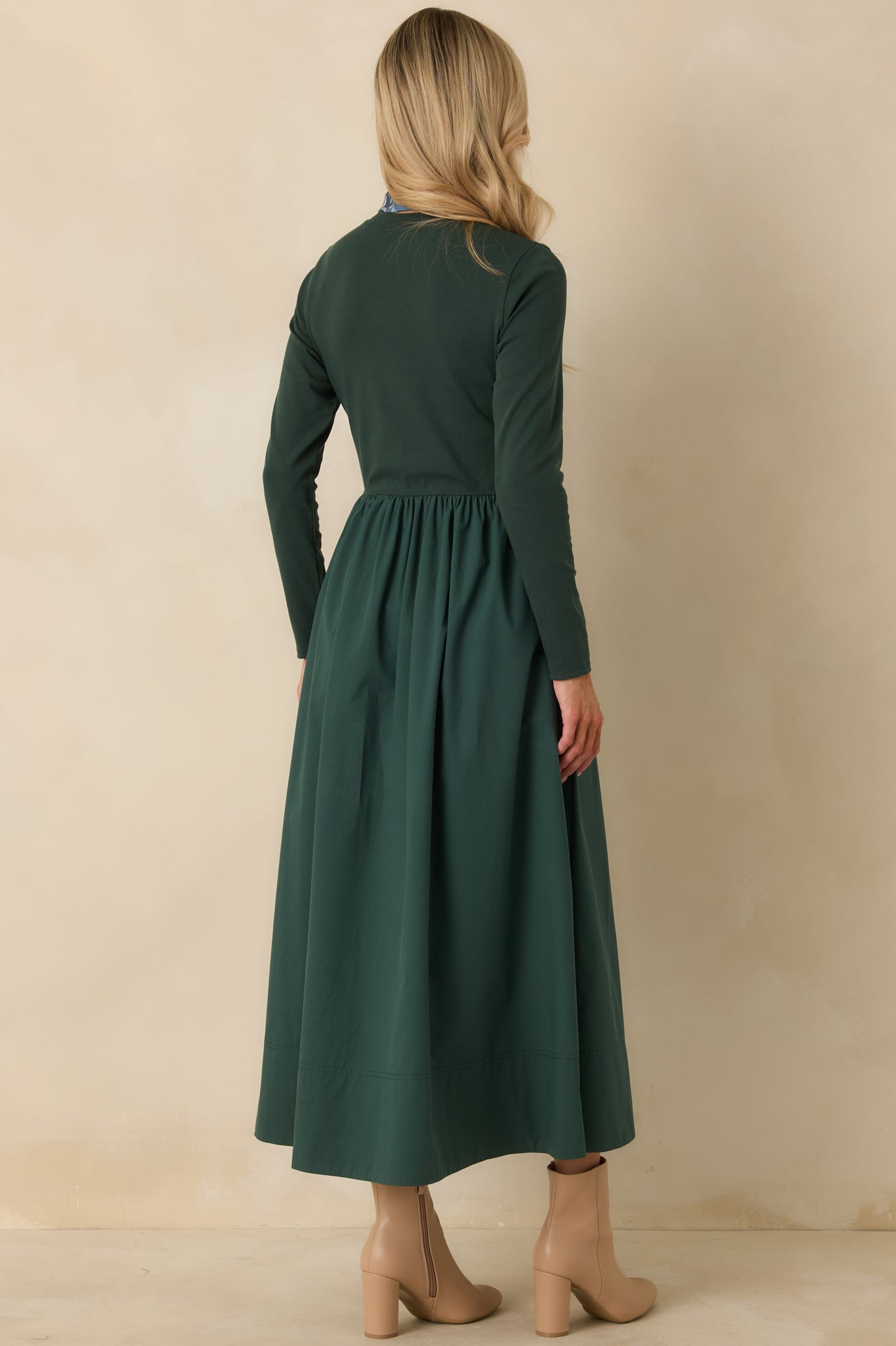 Back view of a green midi dress with a fitted long sleeve knit bodice, gathered waist seam, and voluminous cotton skirt.