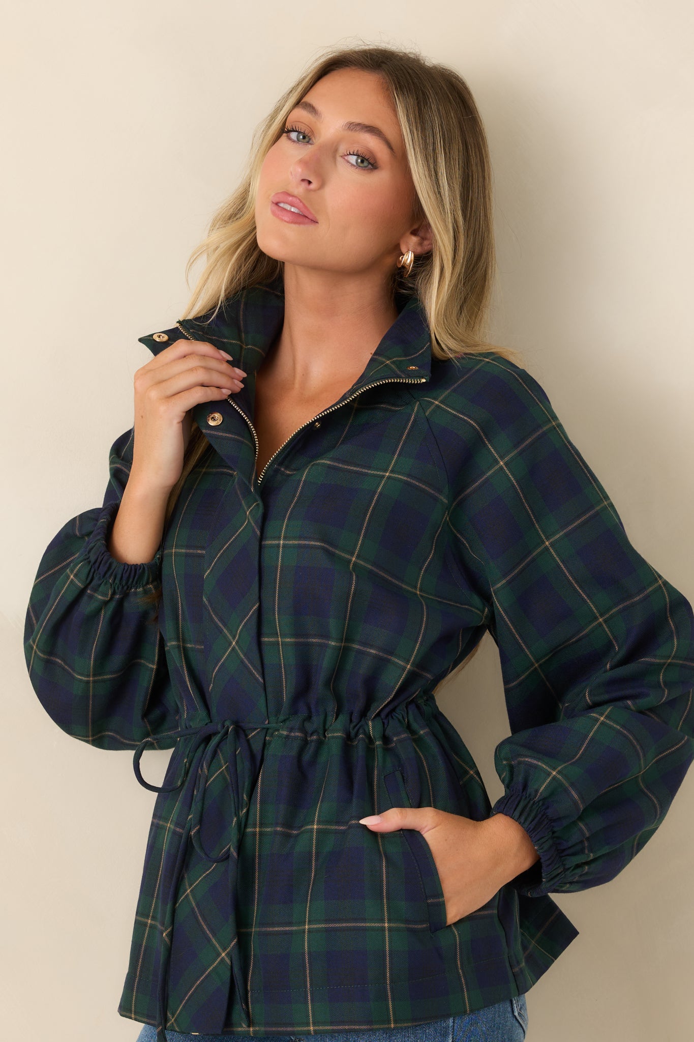 Close view of the green and navy plaid jacket highlighting the oversized patch pocket, defined drawstring waist, and crisp snap accents.