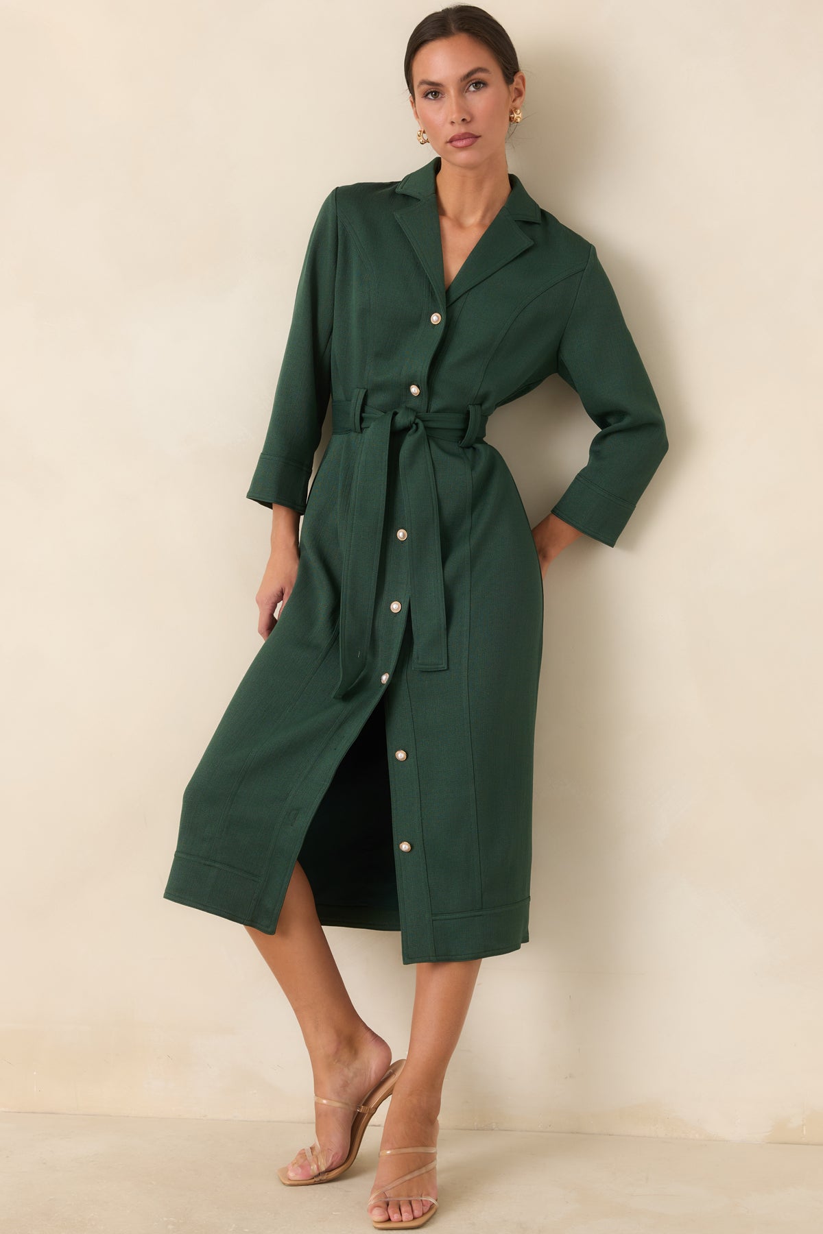 Green dress detail highlighting the round pearl buttons framed in gold-tone metal.