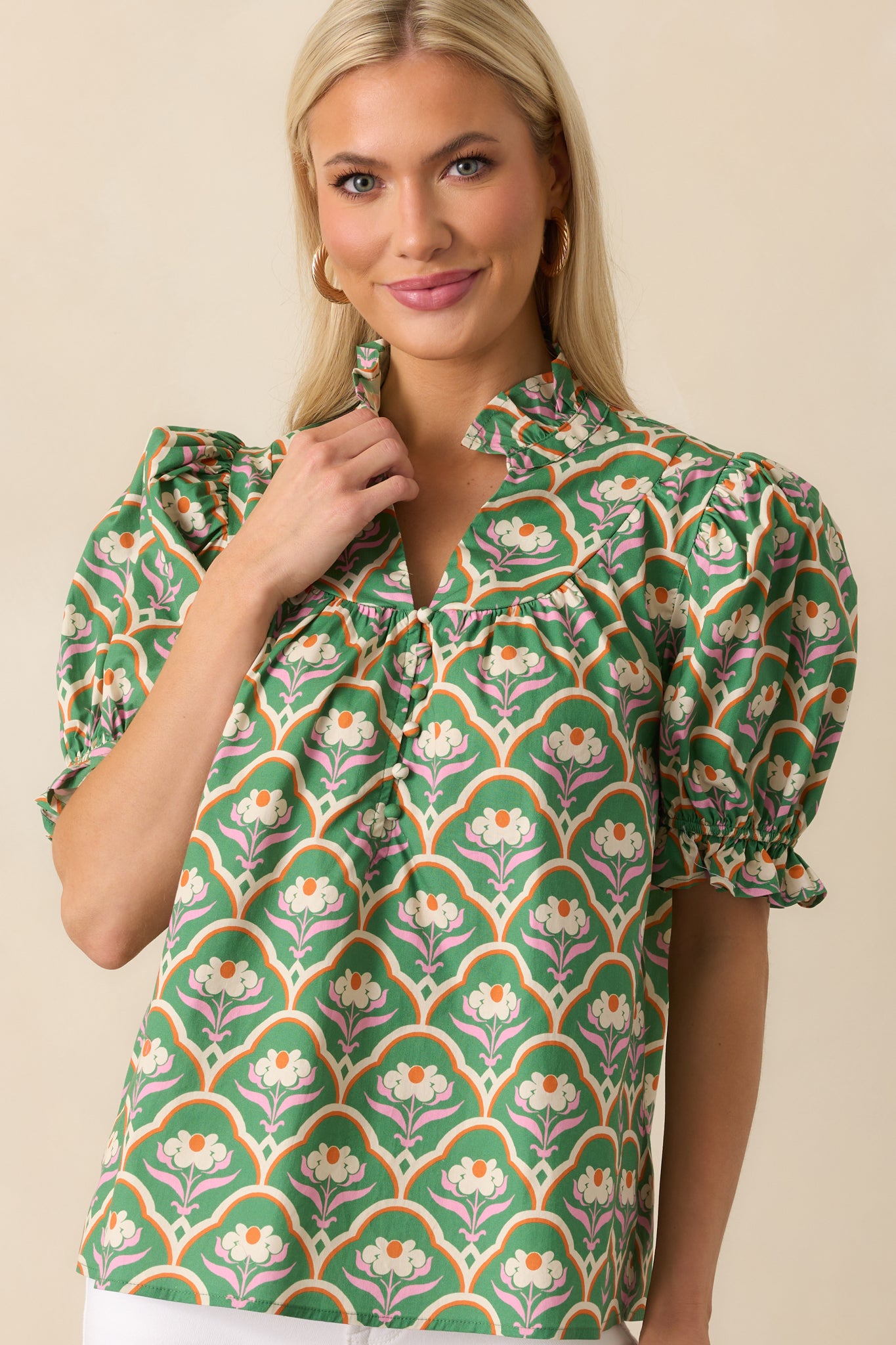 Green top featuring pink multicolor geometric floral print and ruffle notch V-neckline.