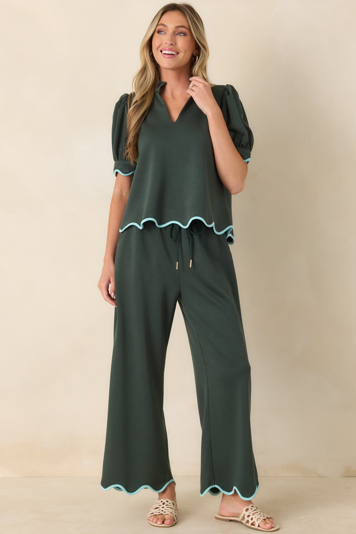 Green top showcasing a tailored split neckline, soft volume sleeves, and feminine scalloped edging.