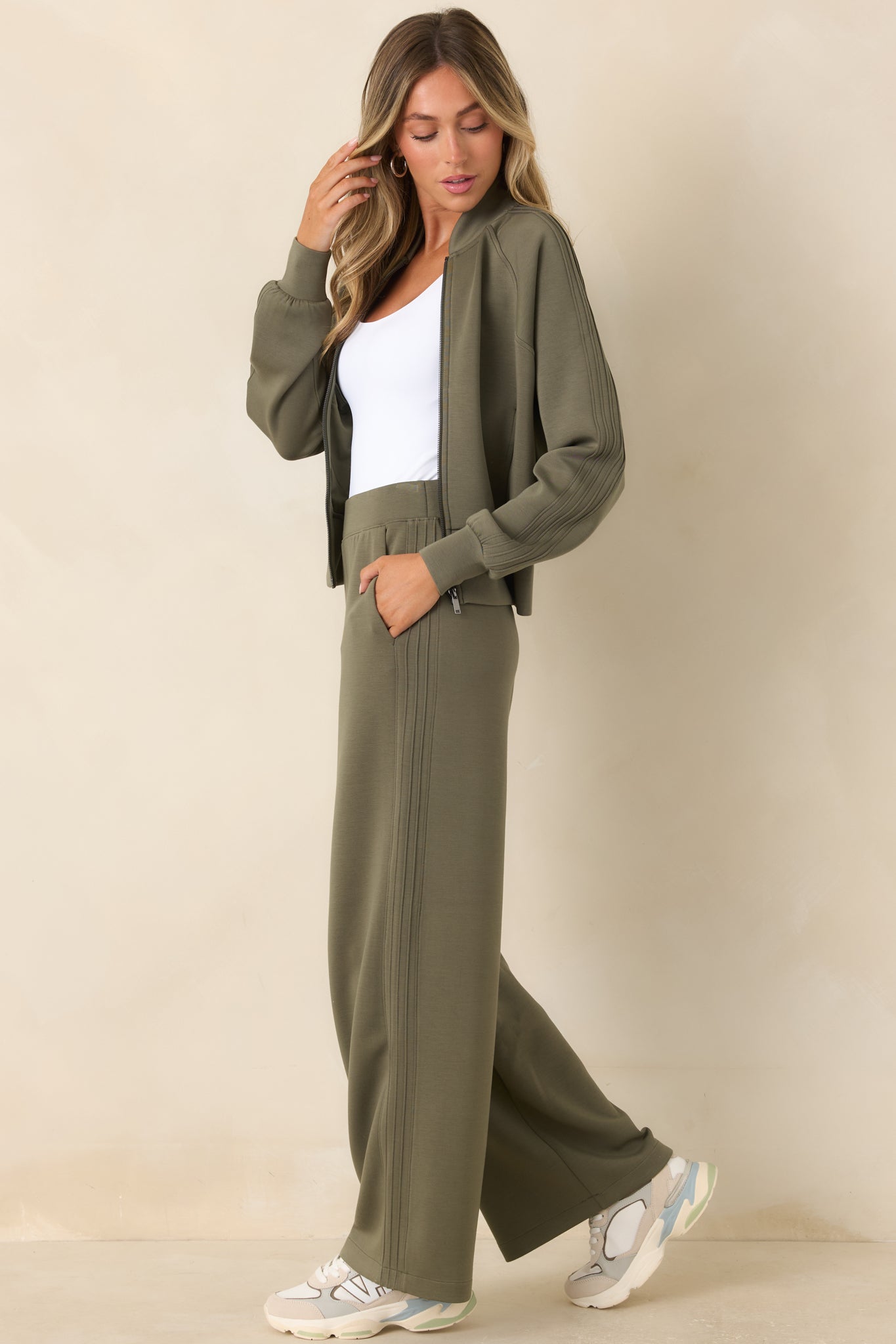 Green wide-leg pants featuring a high-rise fit, sporty pintuck detailing, fluid stretch fabric, and functional side pockets.