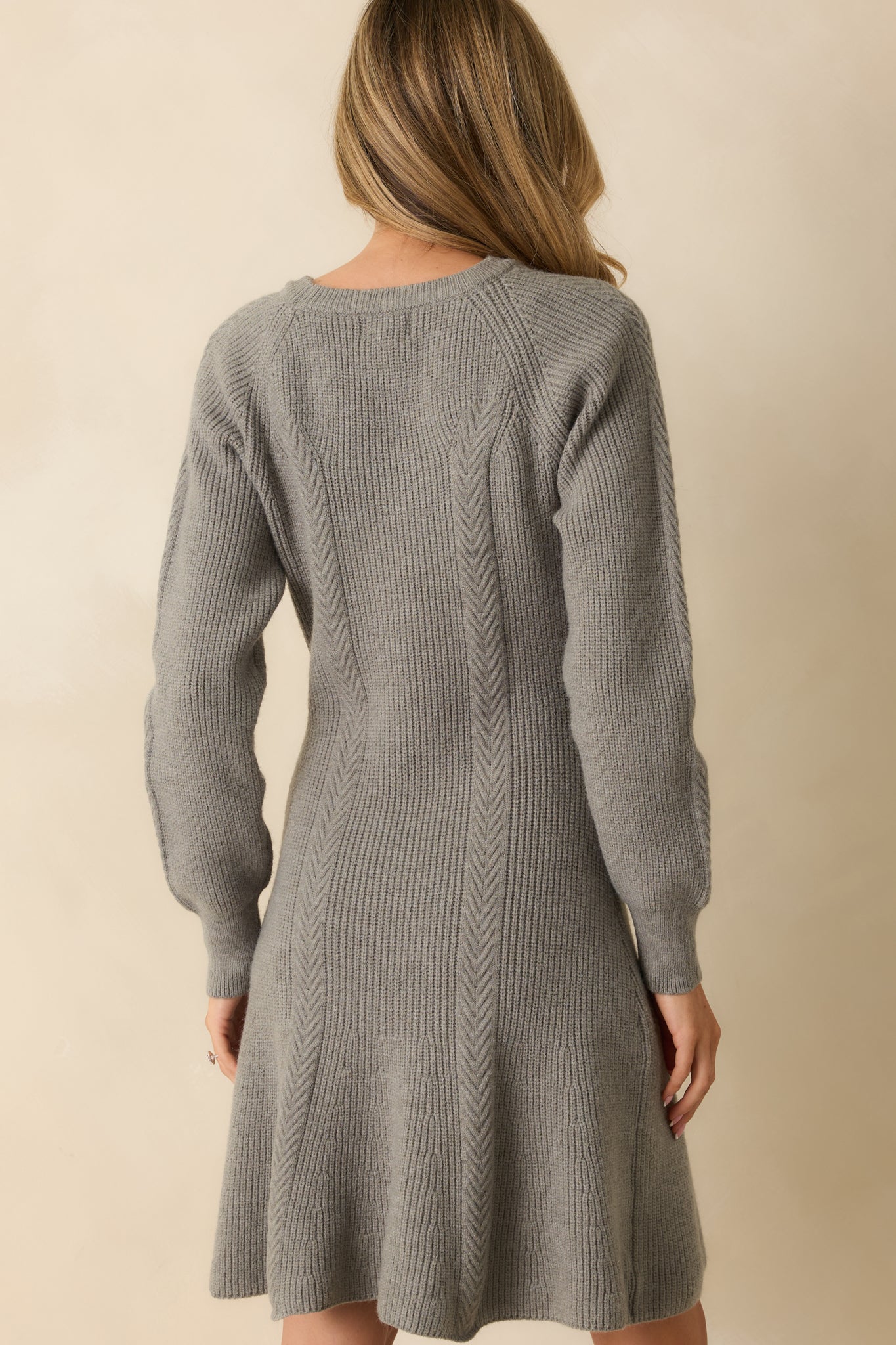 Rear view of grey ribbed knit sweater dress showing fitted bodice, long sleeves, and flared hem.