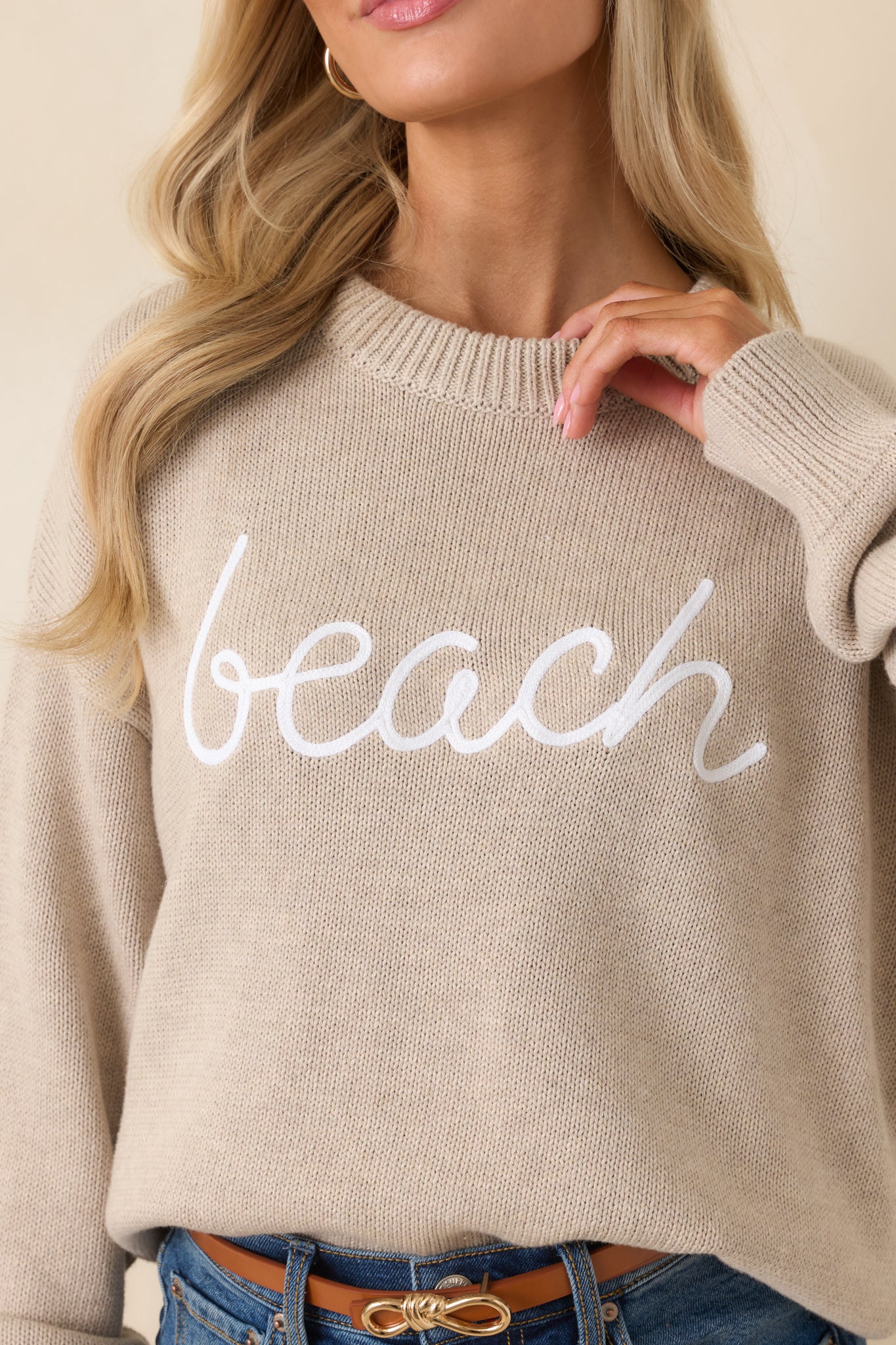 Close-up of raised script “beach” graphic on natural heather cotton knit with visible textured stitching.