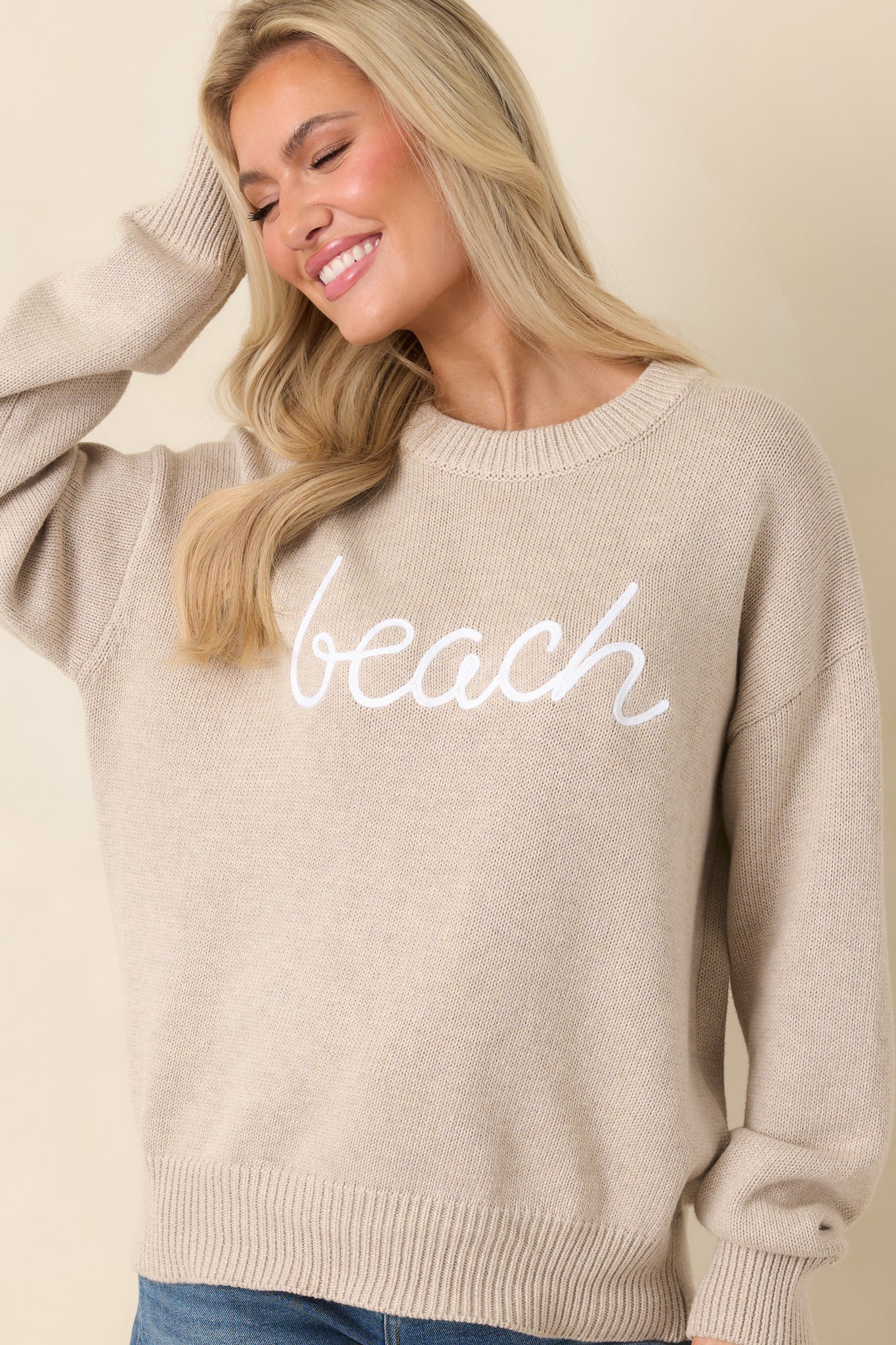Close view of natural heather knit highlighting raised “beach” script and soft cotton texture.
