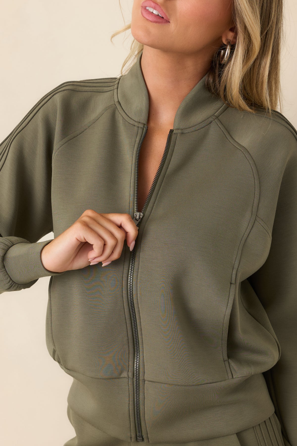 Close-up of the herb green jacket highlighting the full zipper, stand collar, raised pintuck detailing, and soft stretch fabric.