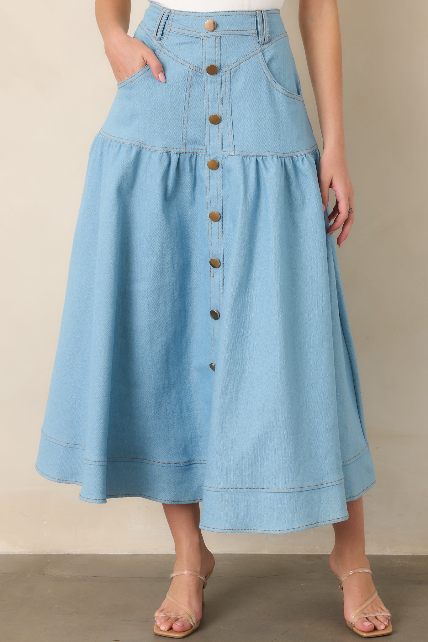 Close view of the high-rise waistband and gold-tone button-down front, highlighting the structured denim construction and contrast stitching.