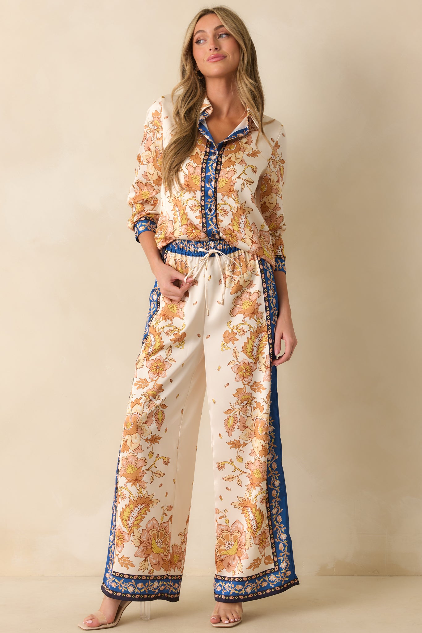 High-rise ivory pants with golden floral pattern, navy border accents, and smooth satin finish.