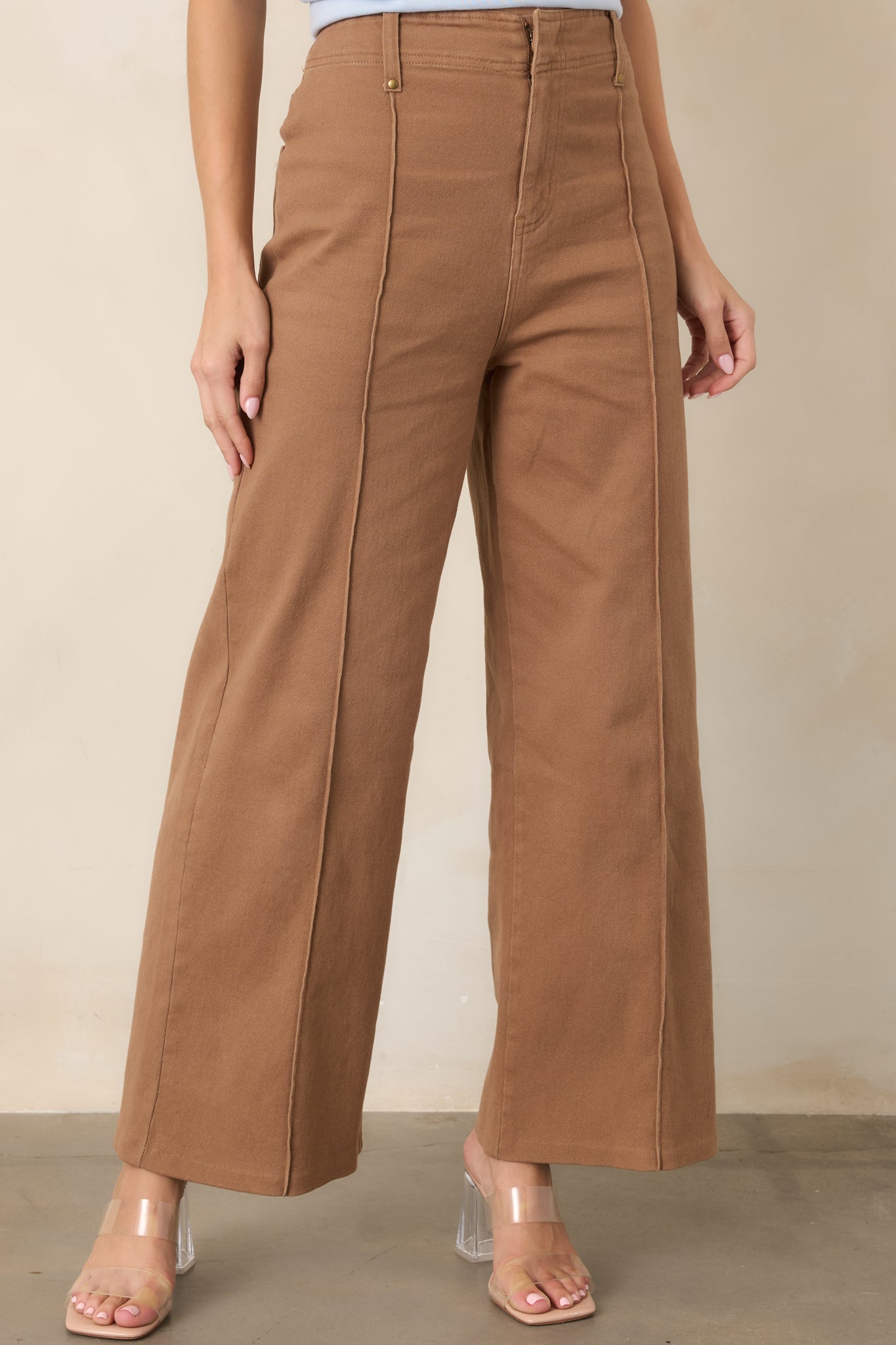 High-rise pants highlighting the structured waistband, functional belt loops, and precisely sewn pleats at the front.