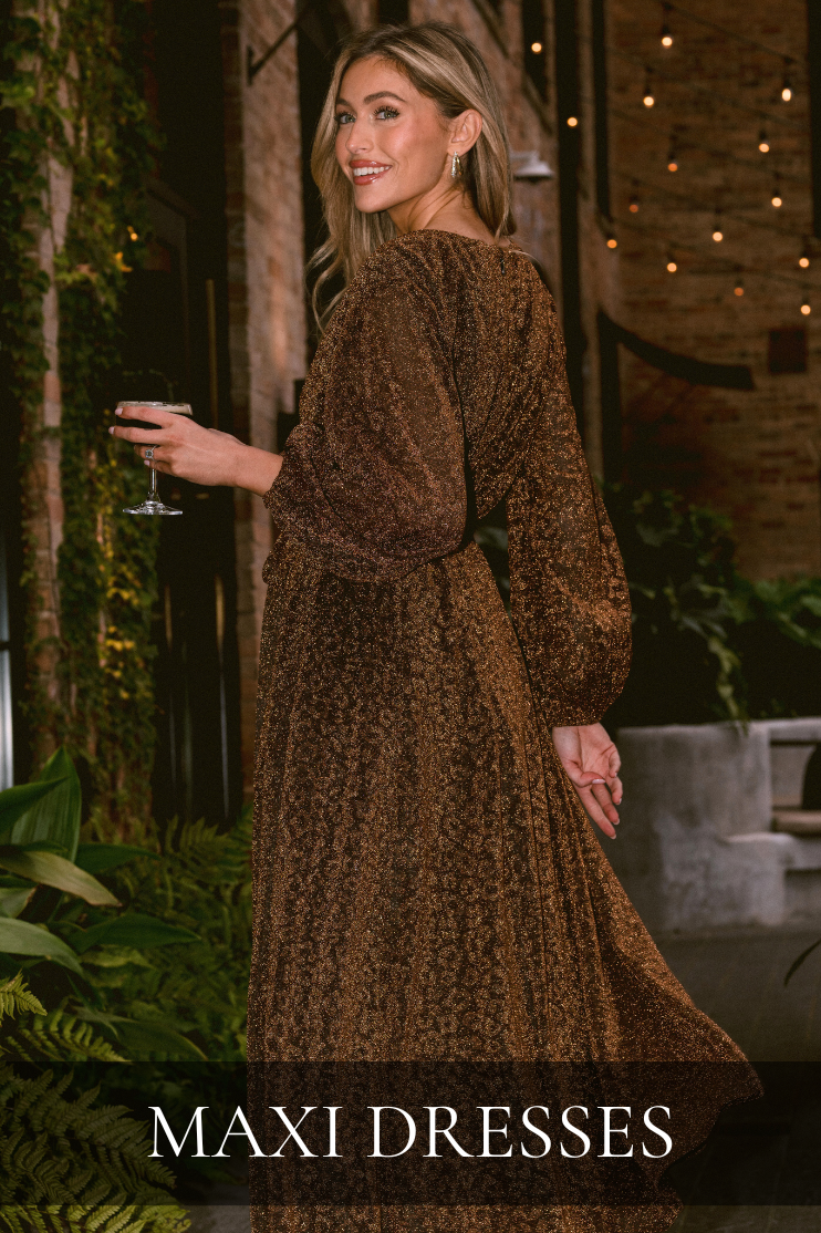 Model wearing a bronze shimmer long-sleeve maxi dress, holding a glass of wine—elegant evening look from the Maxi Dresses collection for women.