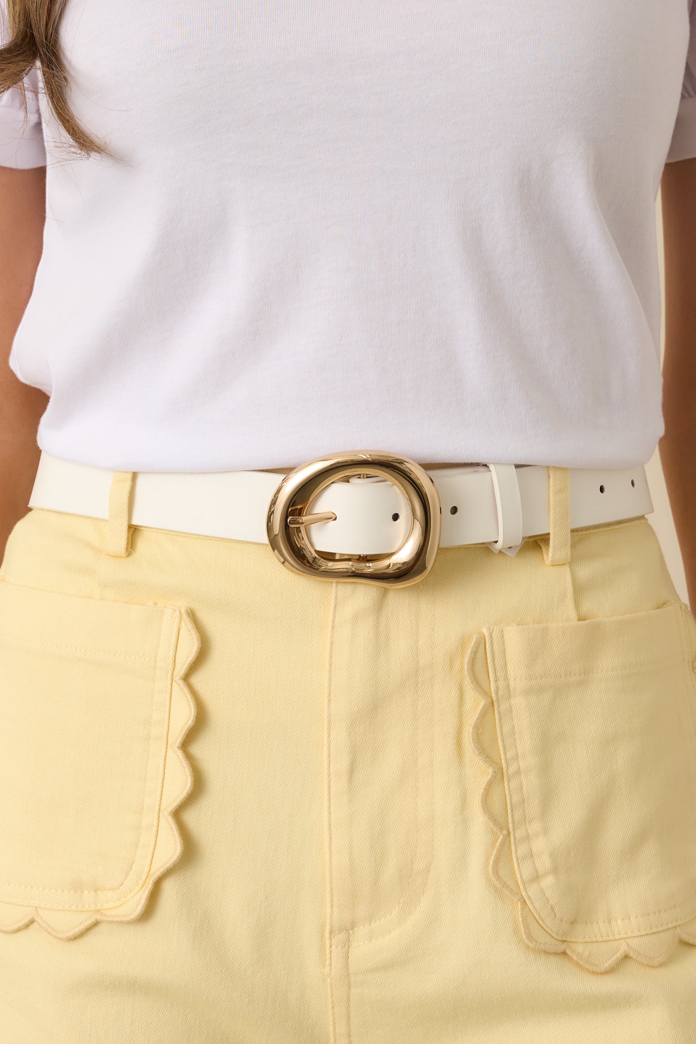 Hollow organic-shaped gold buckle paired with a clean white faux leather strap, highlighting the polished metal finish and adjustable pin closure.