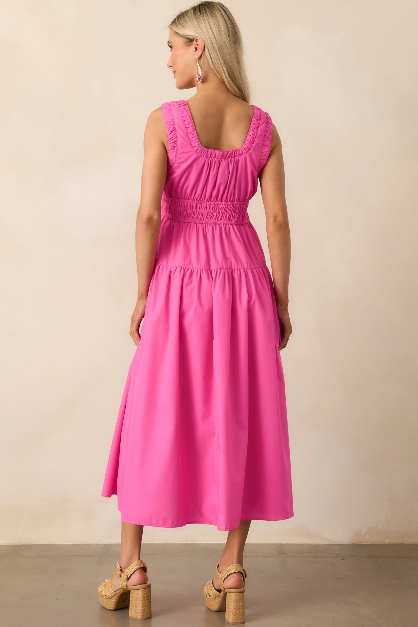 A view from behind of the hot pink midi dress, focusing on the smooth sleeveless back and continued shaping from the ruched waist.