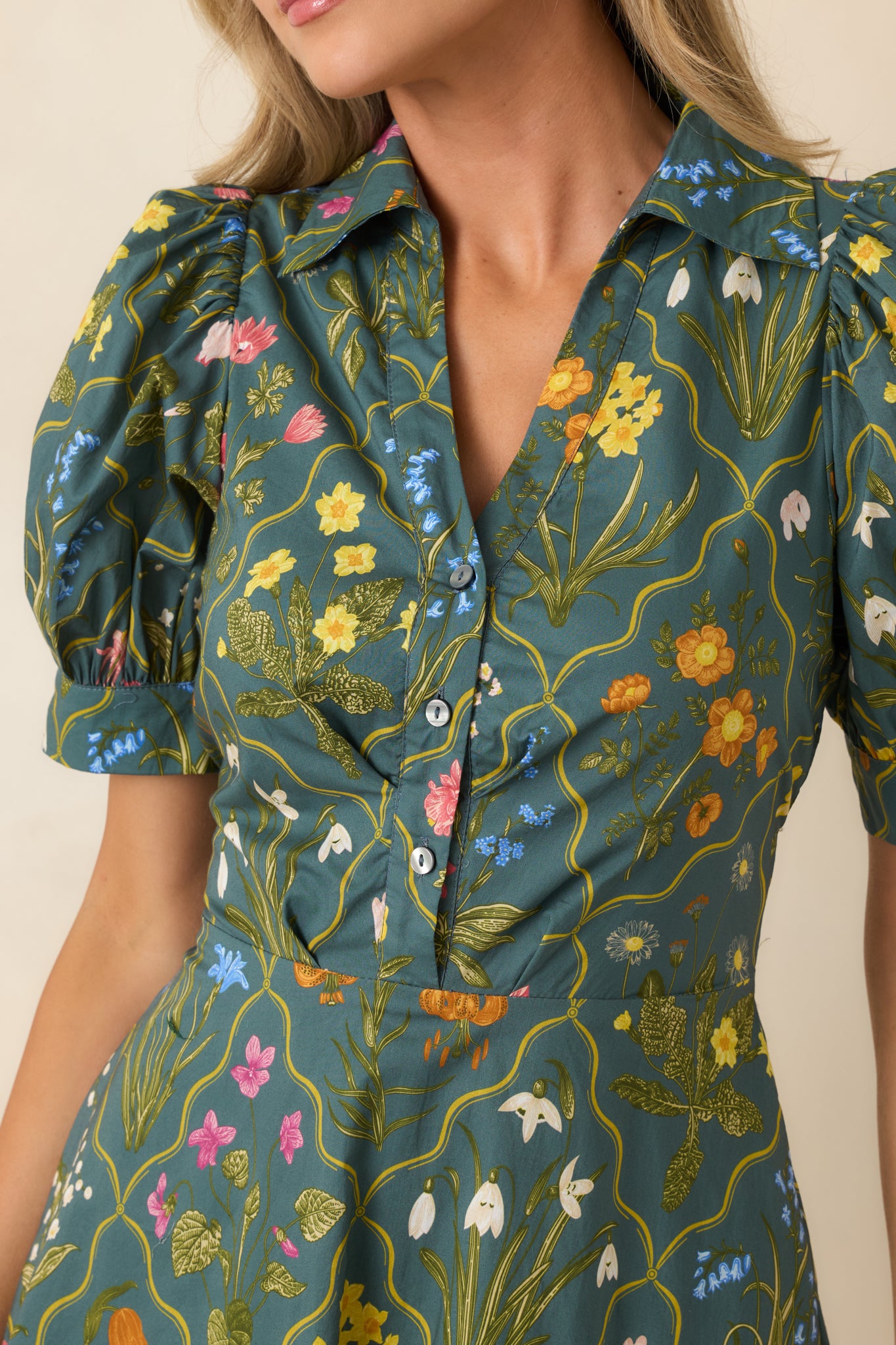 Close-up of the hunter green botanical print highlighting the front buttons, collared V-neckline, and cotton fabric texture.
