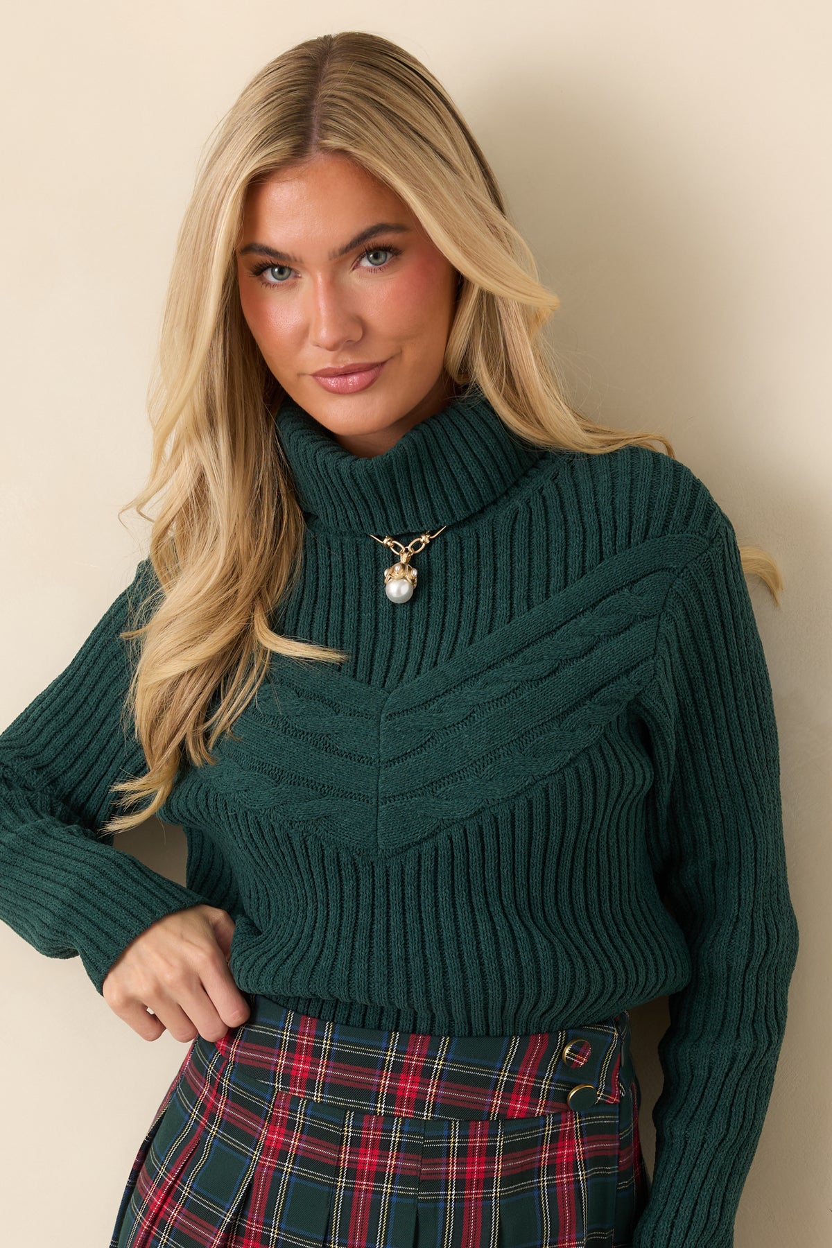 Hunter green sweater highlighting the wide fold-over turtleneck and chevron-shaped cable knit across the chest.
