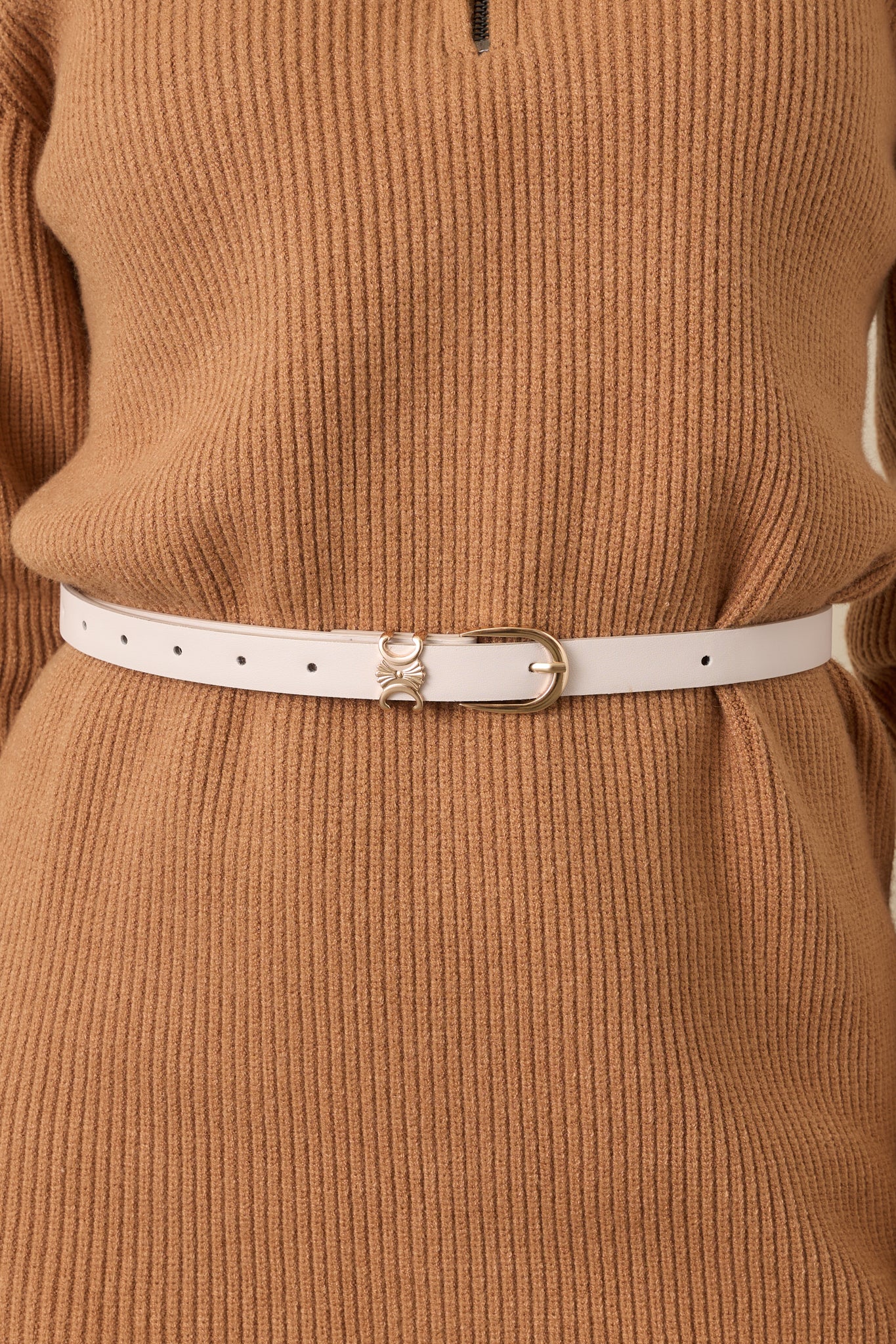 Close-up of the smooth ivory faux leather and polished gold-tone buckle detailing on the slim belt.