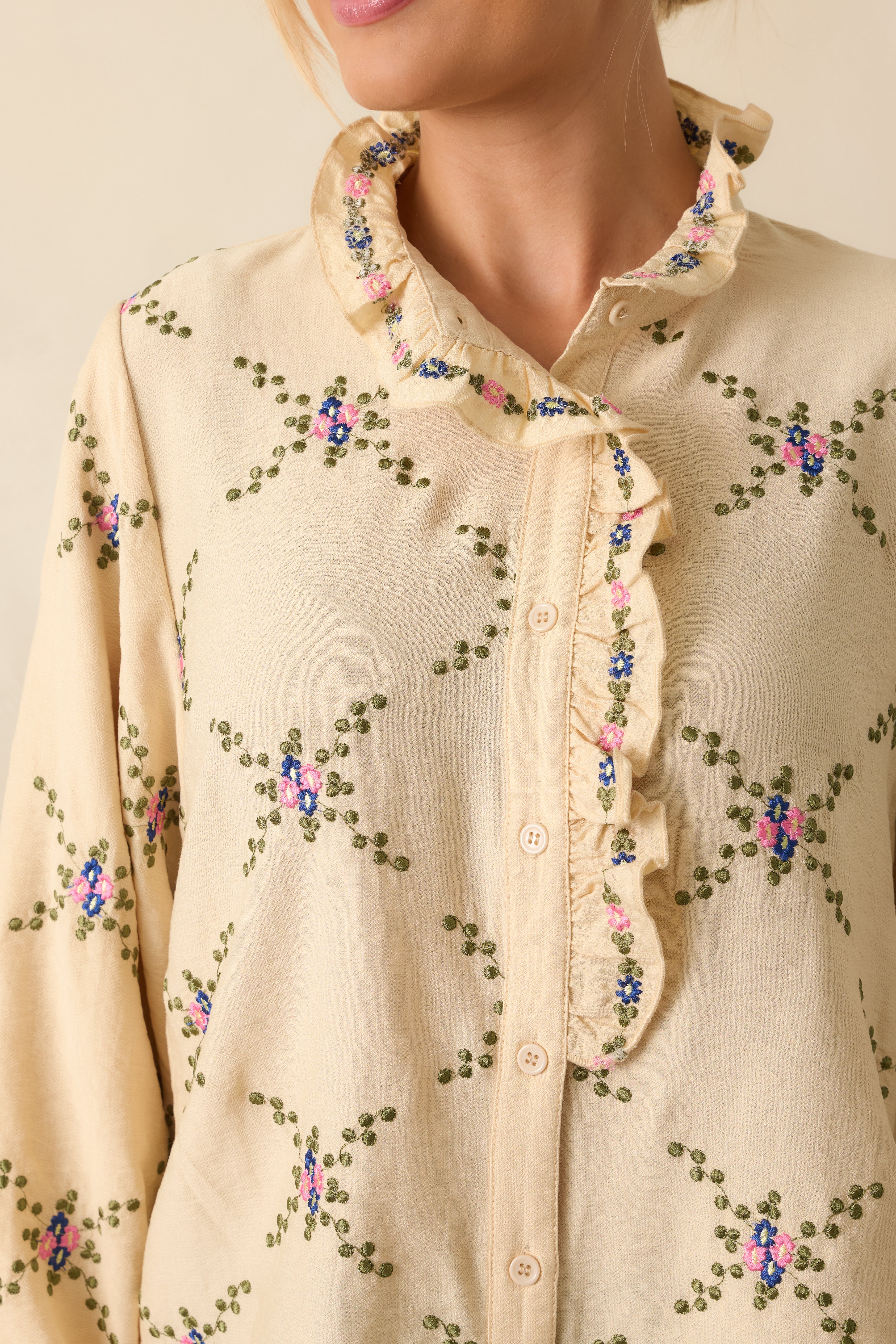 Close-up of the ruffled neckline, button placket, and floral embroidery on the ivory blouse.