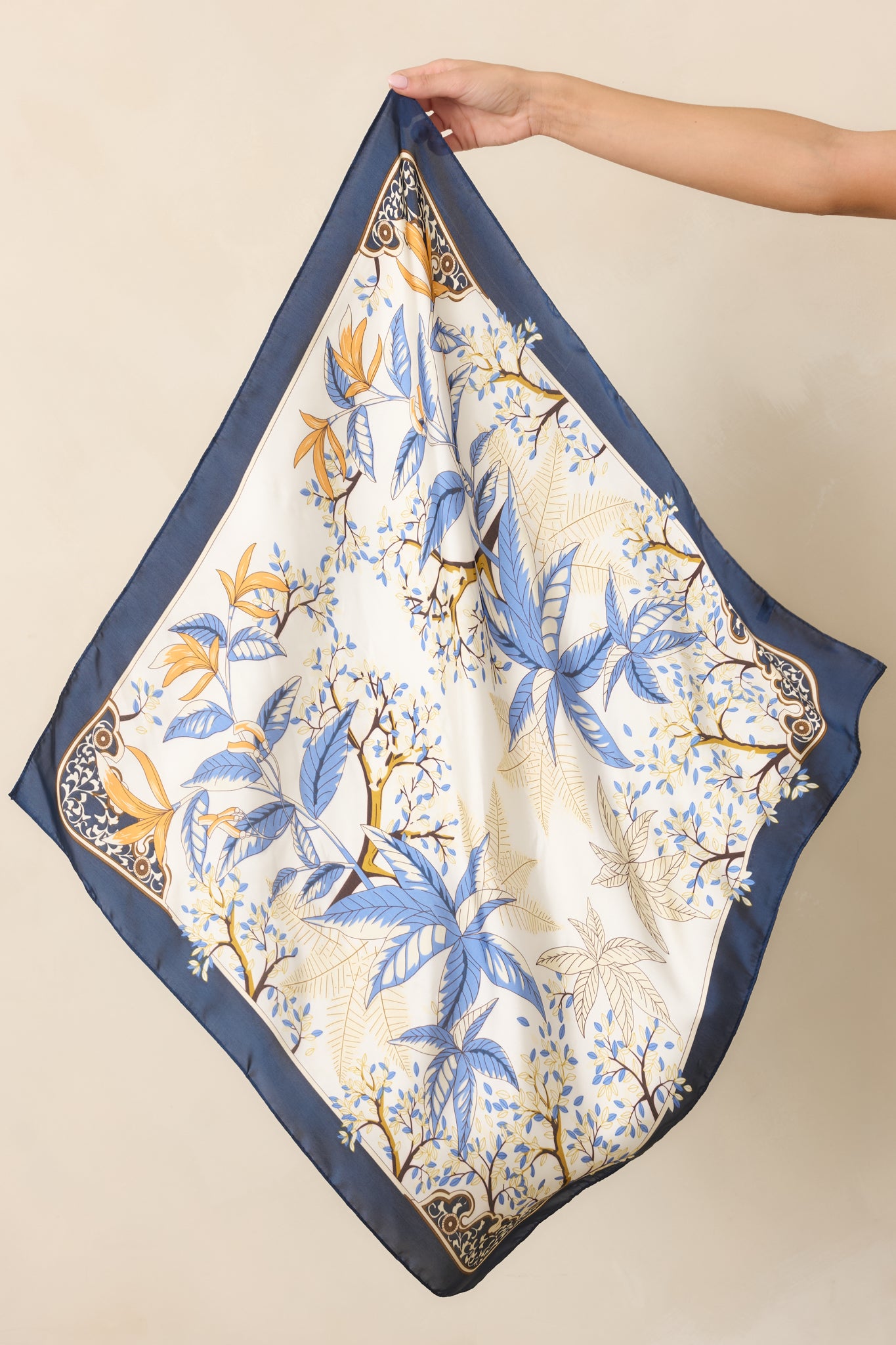 Hair scarf featuring layered blue leaves, delicate branches, golden floral accents, ornate corner details, and a deep navy border on an ivory background.