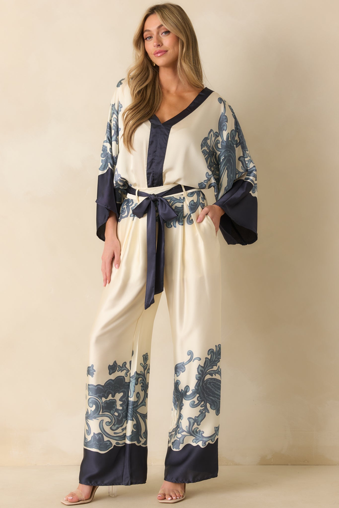 Ivory bodysuit with navy baroque-inspired border print, deep v-neckline, and wide kimono-style sleeves.