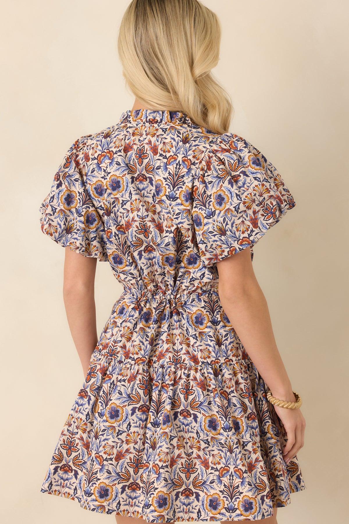Rear of the ivory botanical print mini dress showcases the flutter sleeves, adjustable drawstring waist, and tiered skirt.