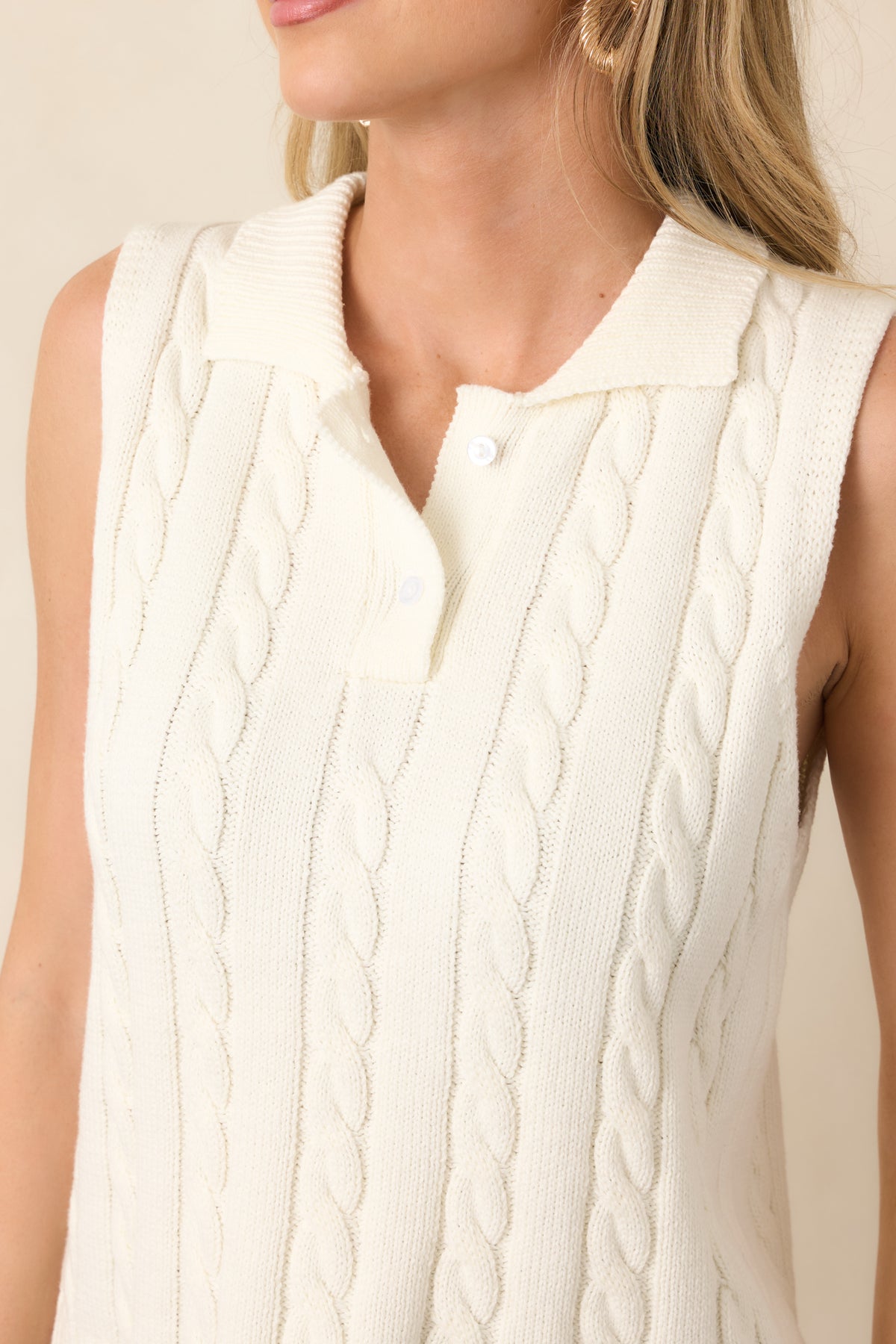 Close-up of the ivory cable-knit fabric, featuring dimensional braided texture, functional buttons, and neatly finished ribbed detailing.