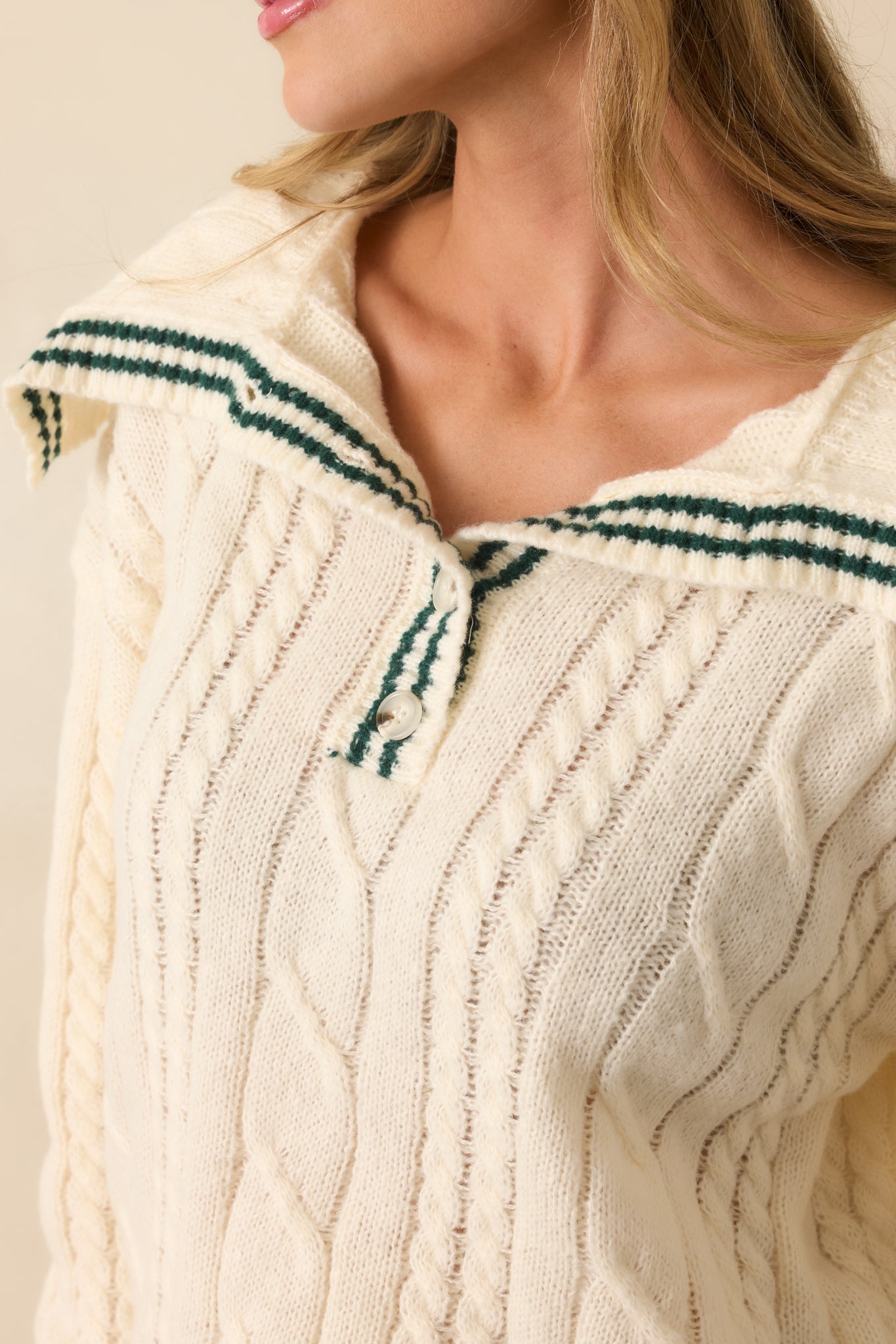Tight detail showing the ivory cable knit pattern, hunter green stripe trim, and quarter button closure.