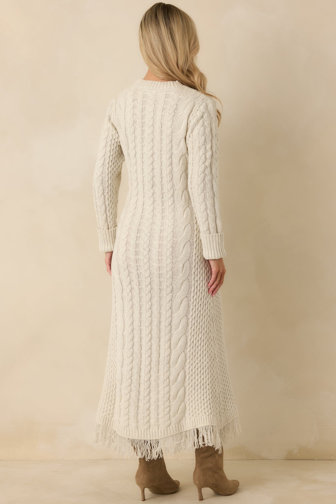 Back of ivory cable knit maxi dress featuring vertical textured patterns, long sleeves, ribbed cuffs, and fringe hem.