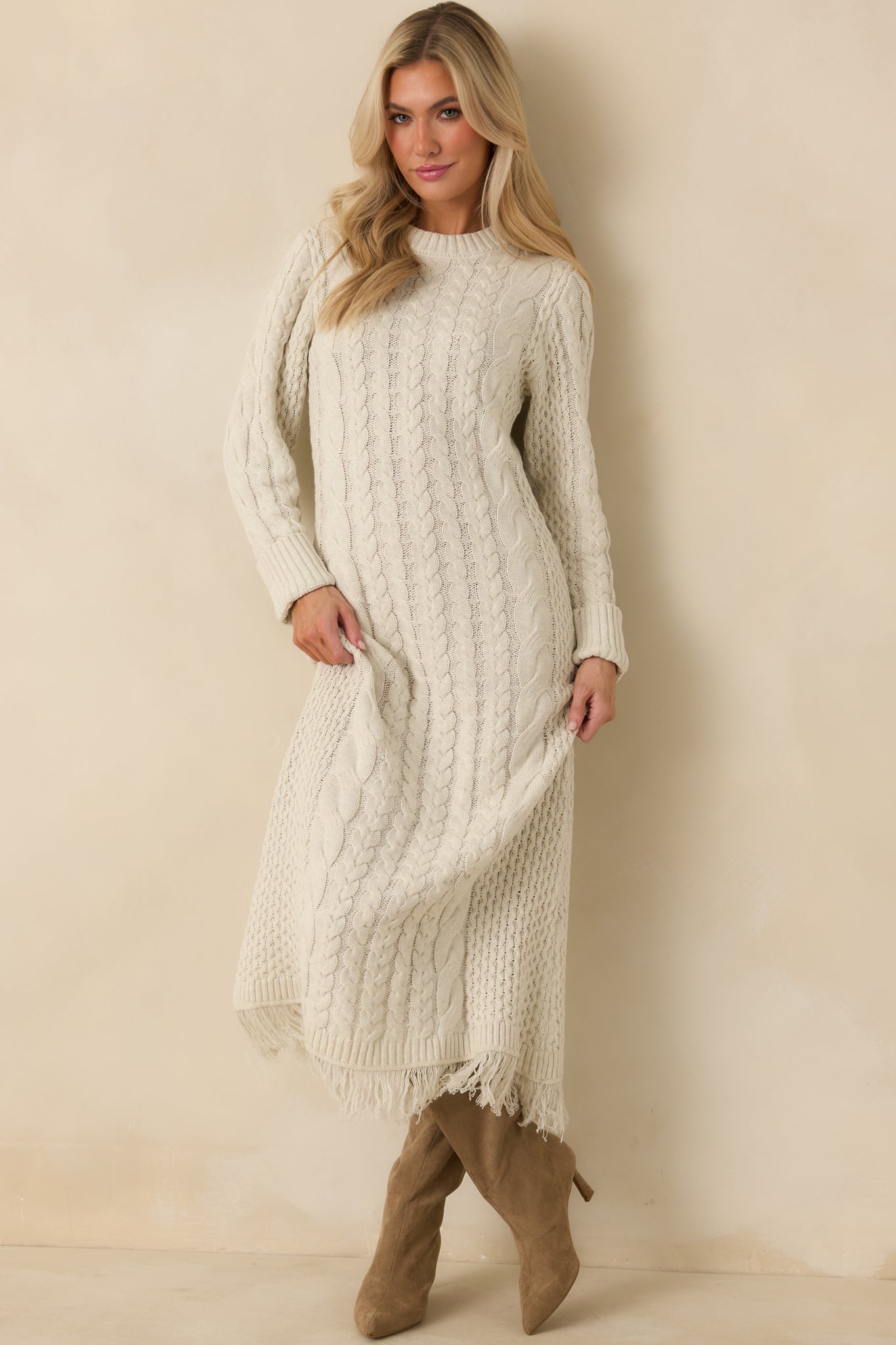 Ivory cable knit maxi dress with a ribbed crew neckline, long sleeves, folded cuffs, and fringe hem.