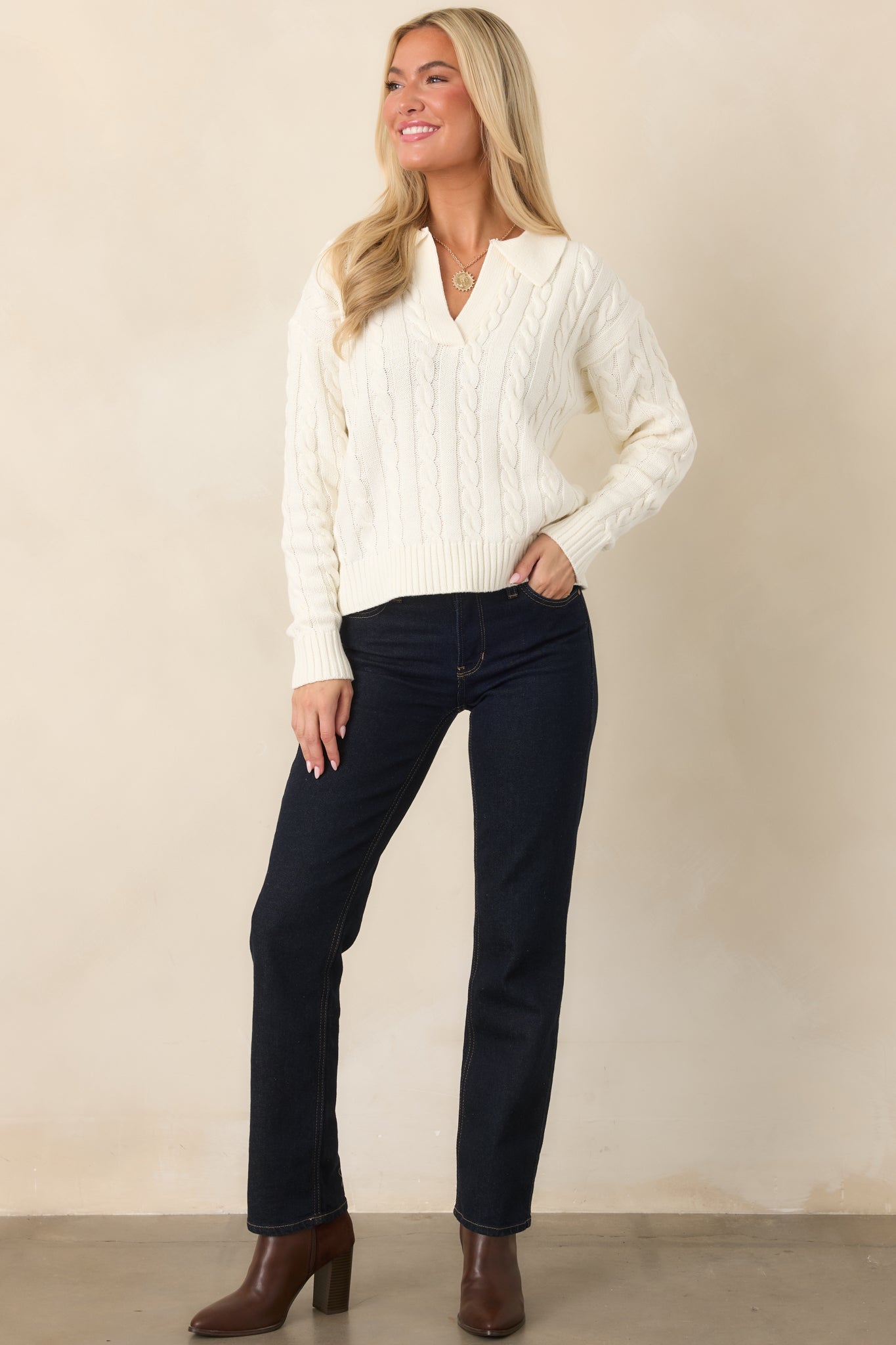 Ivory knit pullover featuring a prominent cable pattern, buttoned collar, straight hem, and ribbed sleeve openings.