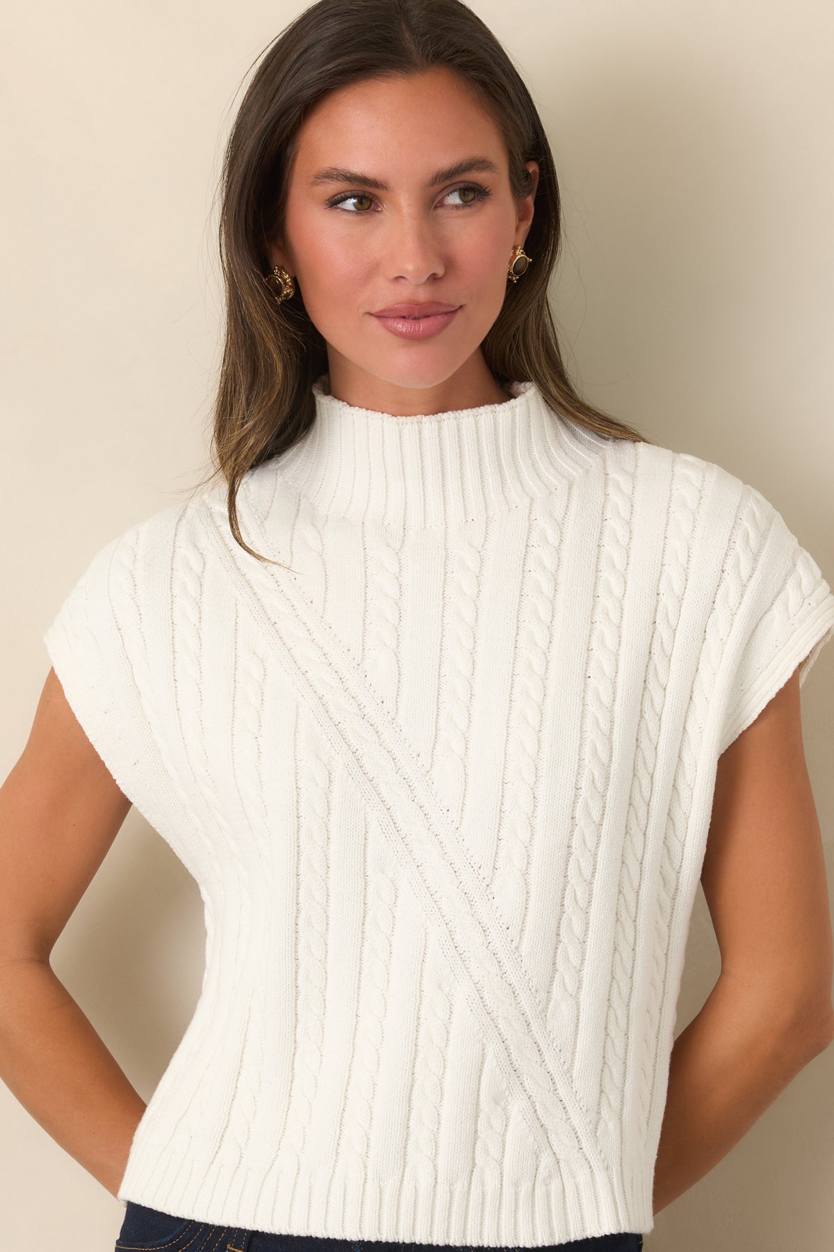 Ivory sleeveless sweater features a structured cable-knit pattern, mock neckline, and relaxed silhouette with ribbed trim.