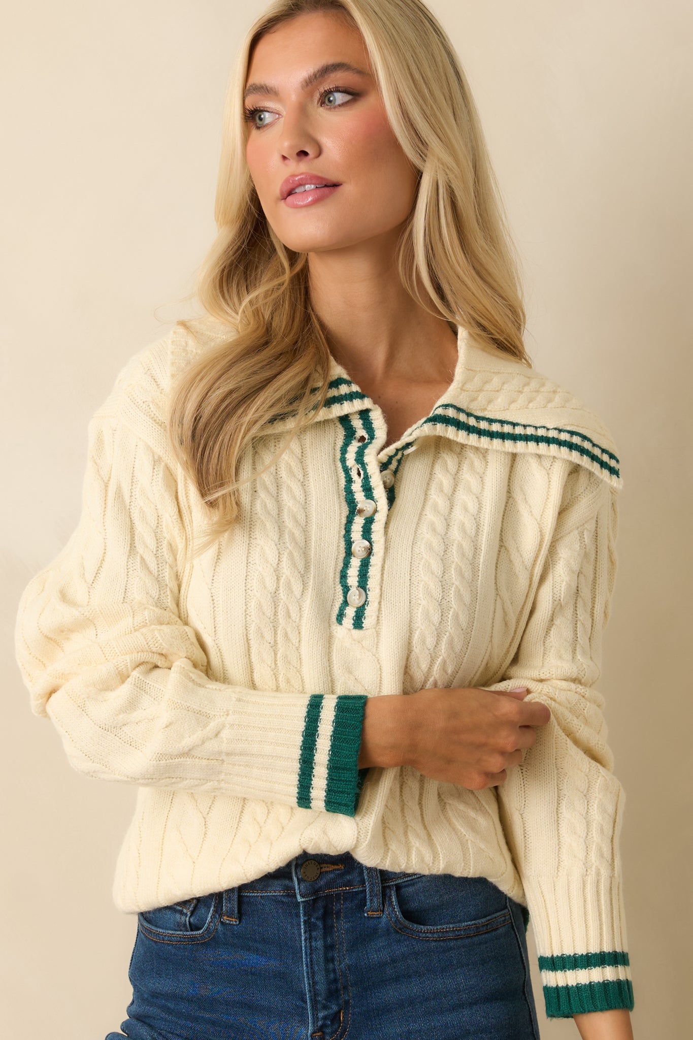 Ivory cable knit sweater with collared neckline featuring contrast green trim, partial button placket, long sleeves, and ribbed cuffs and hem.