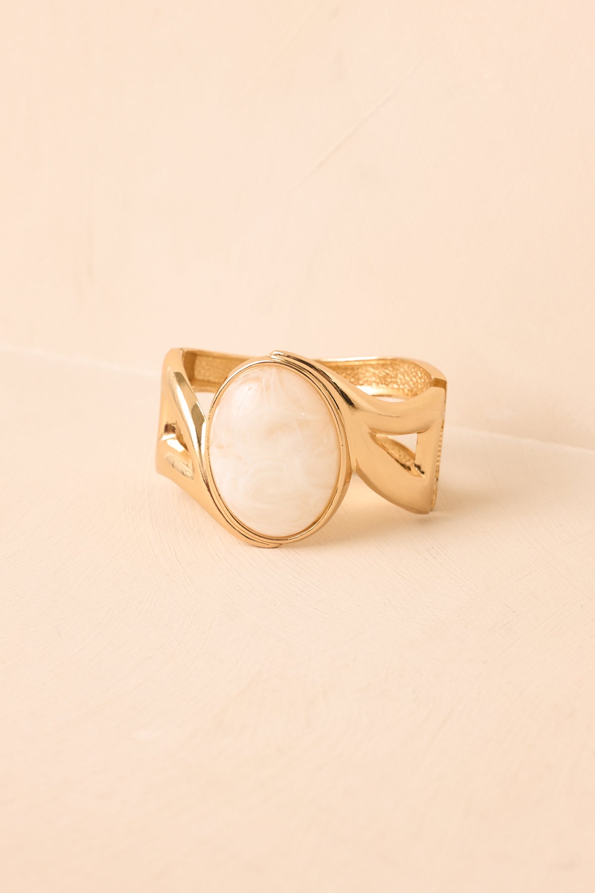 Ivory cabochon bracelet against a beige backdrop, featuring a sculptural open cuff with polished geometric detailing.