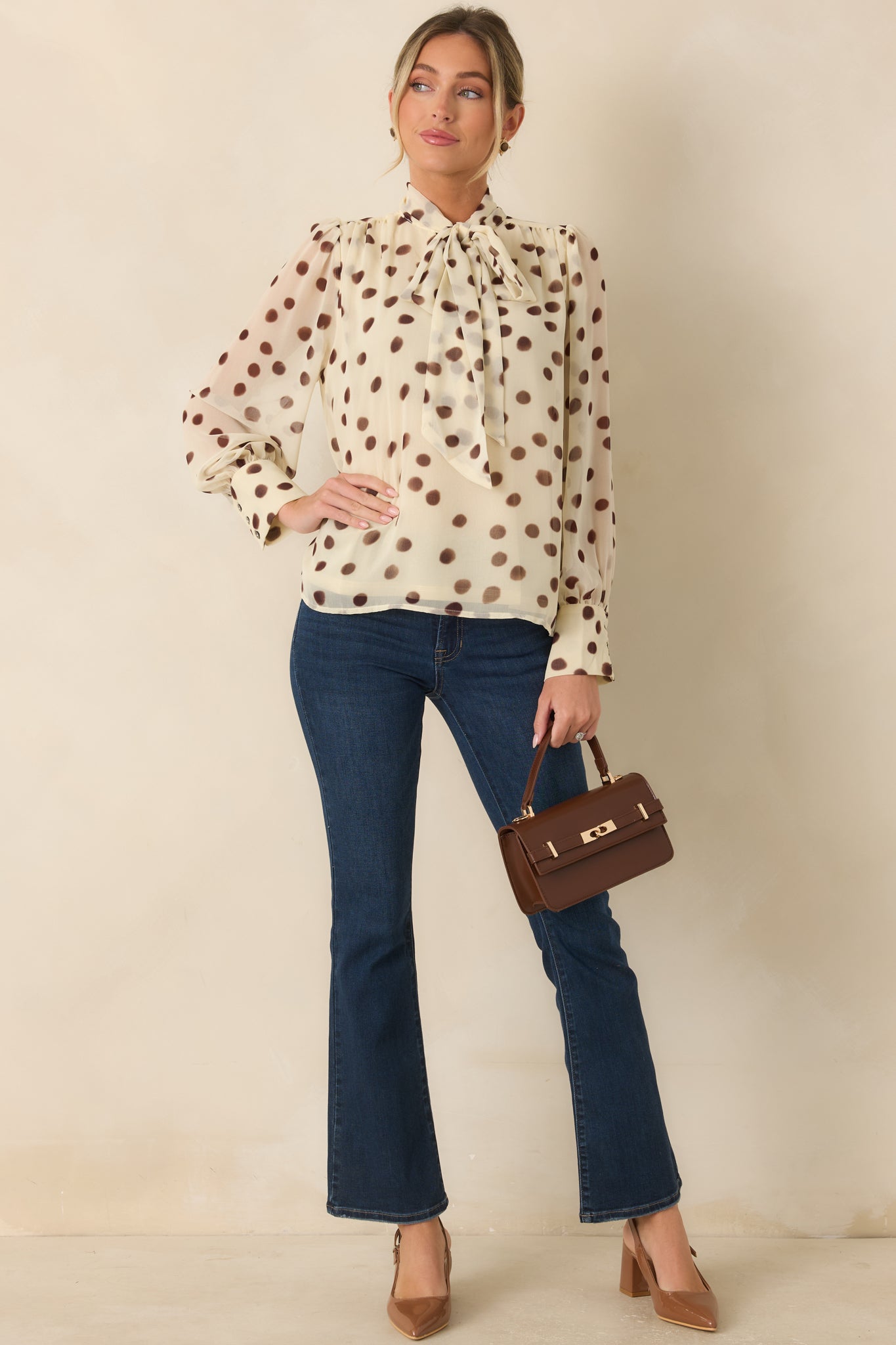 Ivory chiffon blouse featuring painterly brown polka dots, a self-tie neckline, gathered shoulders, and long sleeves with buttoned cuffs.