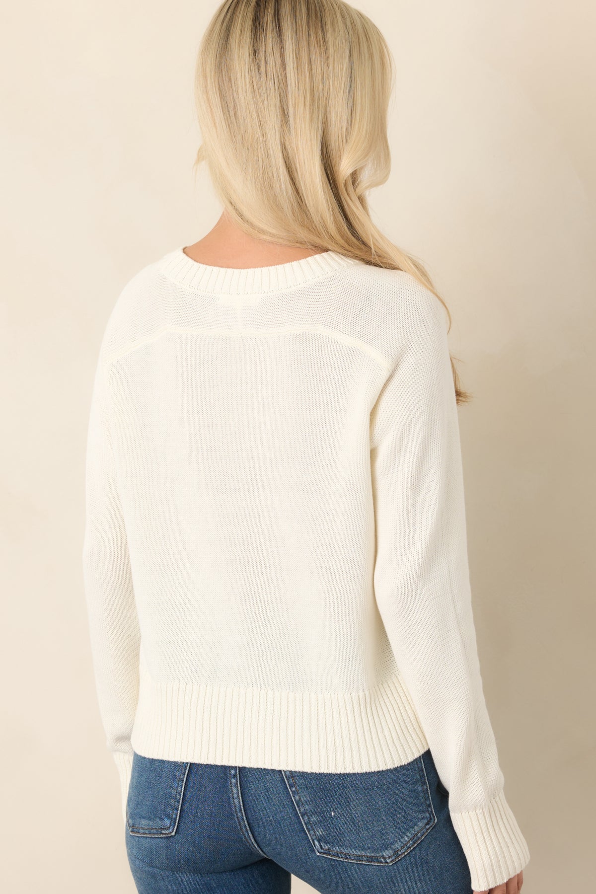 Rear view of the ivory cotton knit top featuring its relaxed slightly cropped silhouette, long sleeves, and ribbed neckline and hem.