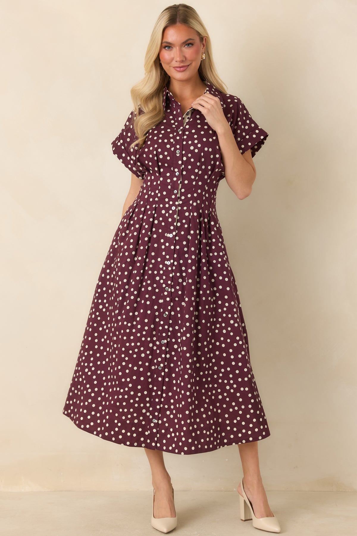 Ivory cotton dress accented with plum polka dots, short sleeves, a defined button-front bodice, and a flowing fit-and-flare midi skirt.
