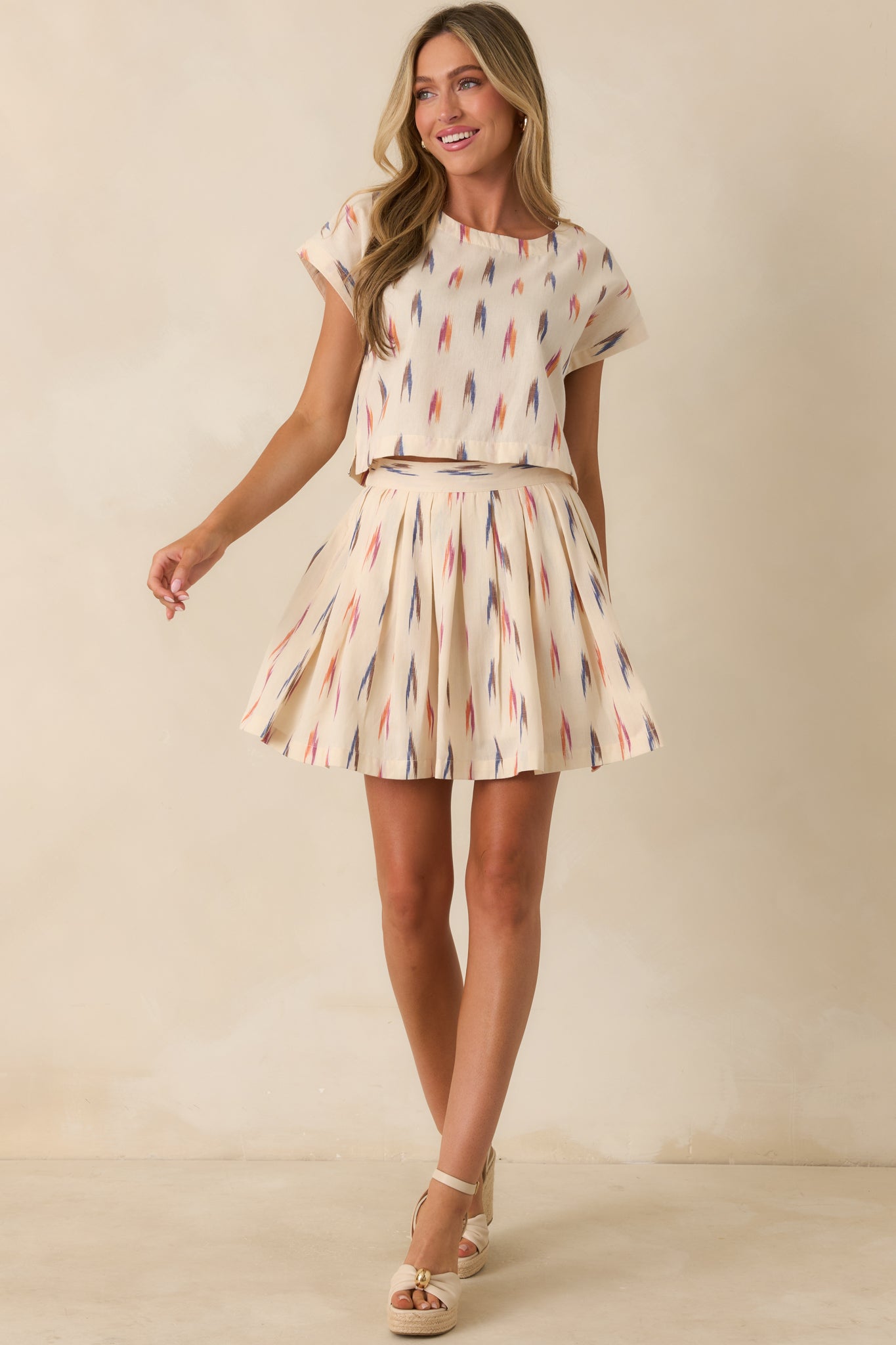 Ivory cropped top with dolman cap sleeves and multicolored graphic print.
