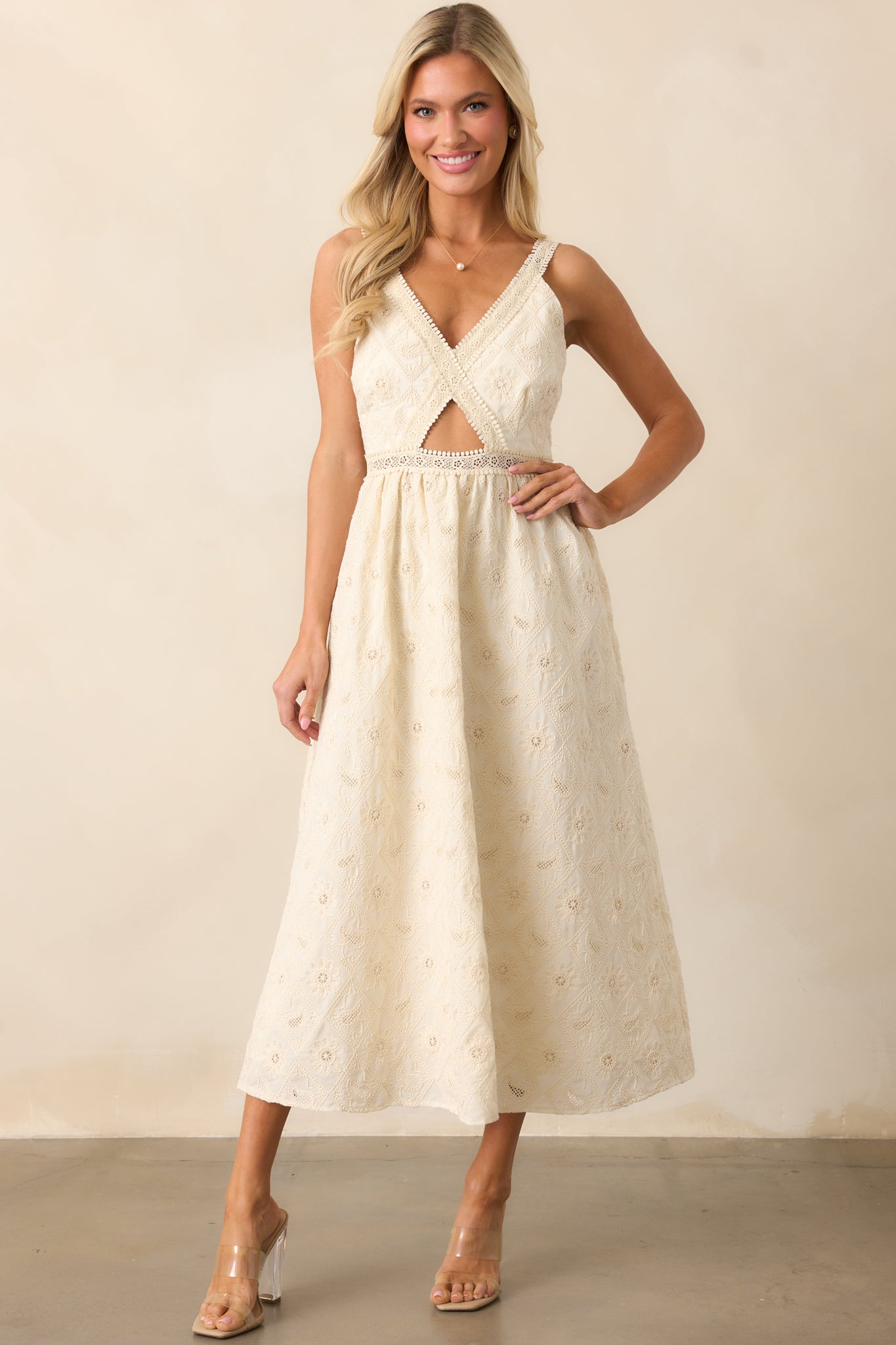 A delicate ivory dress with intricate lace embroidery detailing throughout, featuring a v-neckline, a central bodice cutout, and adjustable straps for a customizable fit.