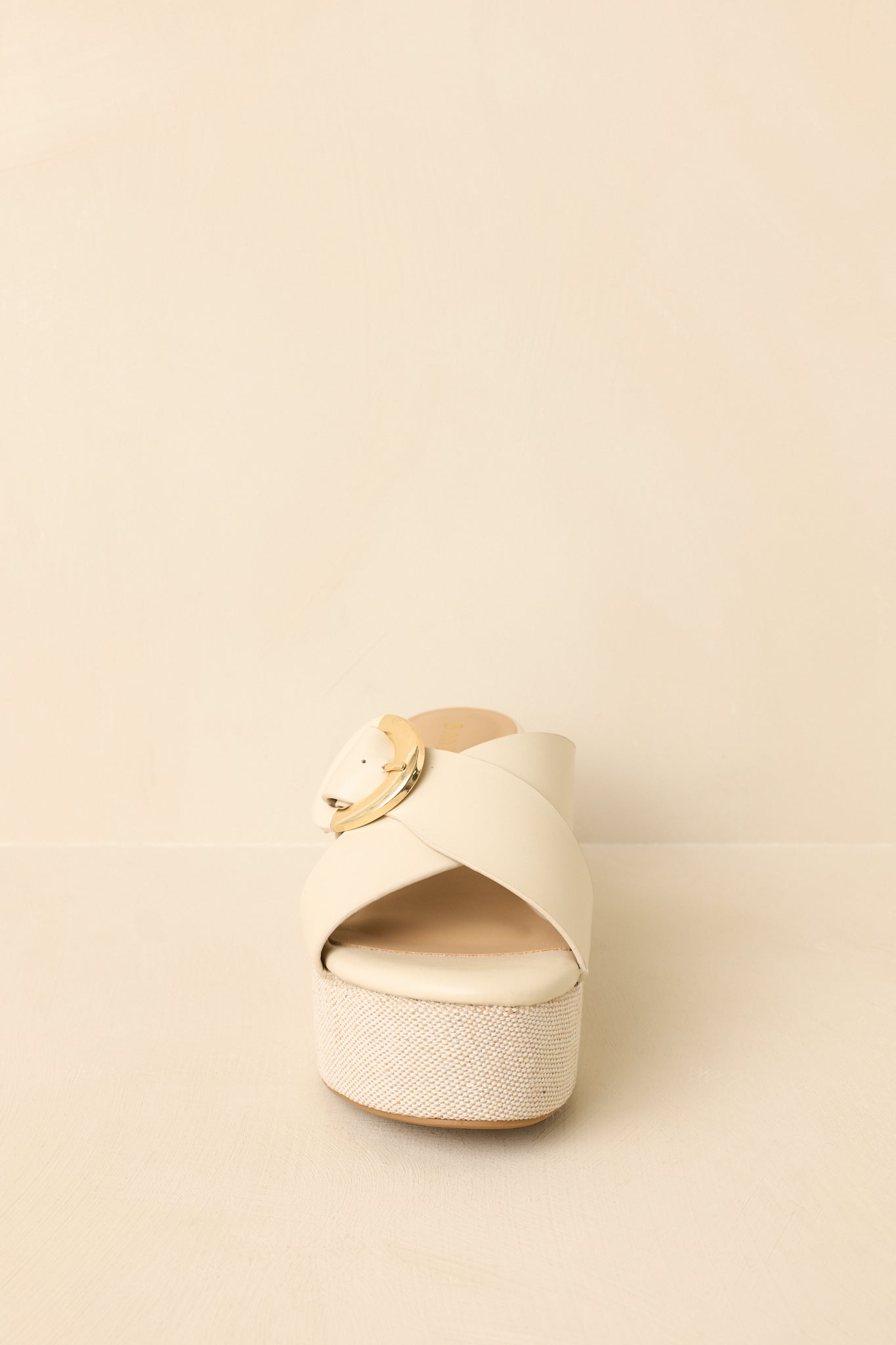 Front view of ivory faux leather wedges on a beige background highlighting the wide strap and statement buckle.