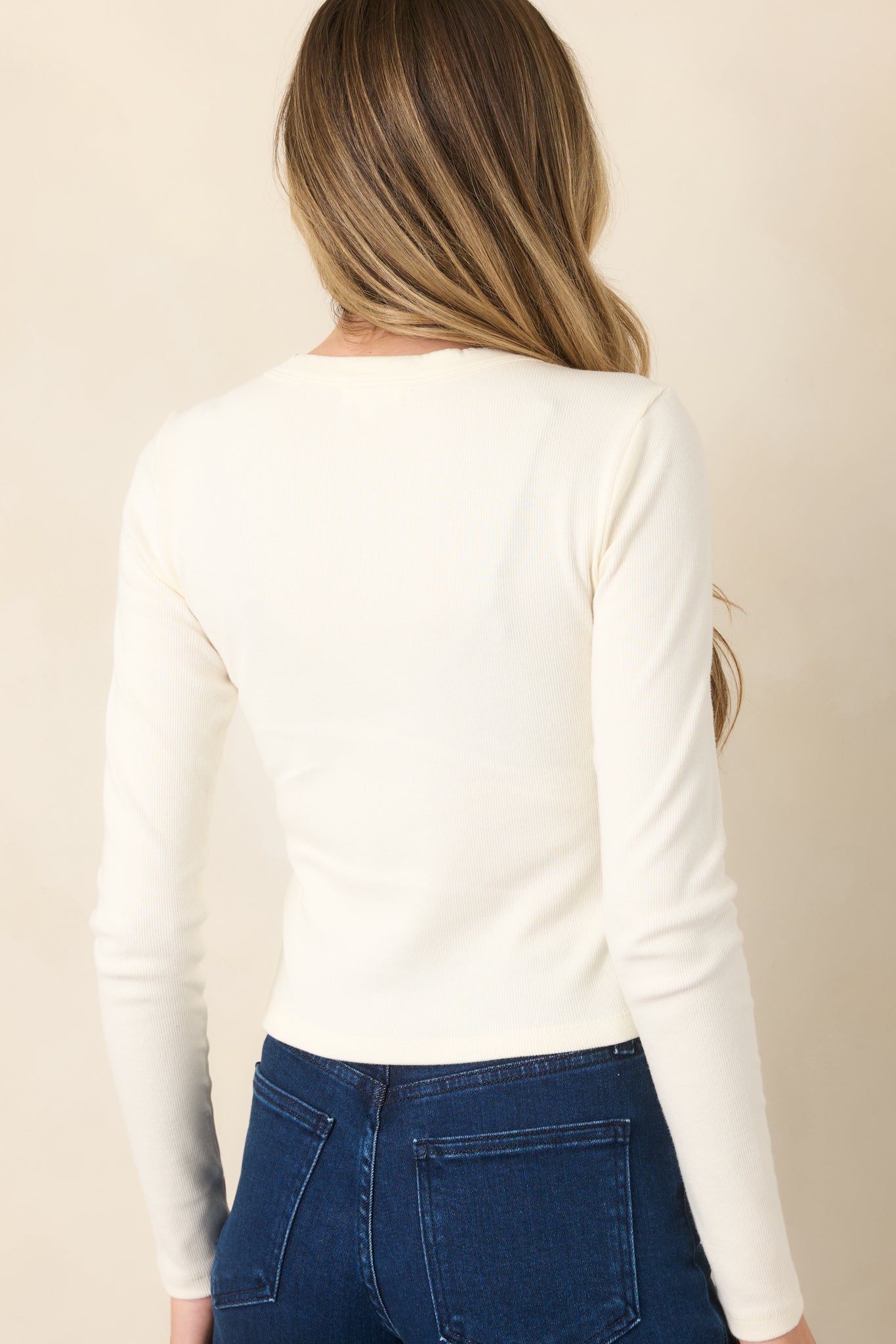 Rear view of the ivory top showing its close-to-body silhouette, long sleeves, and cropped waist-length hem.