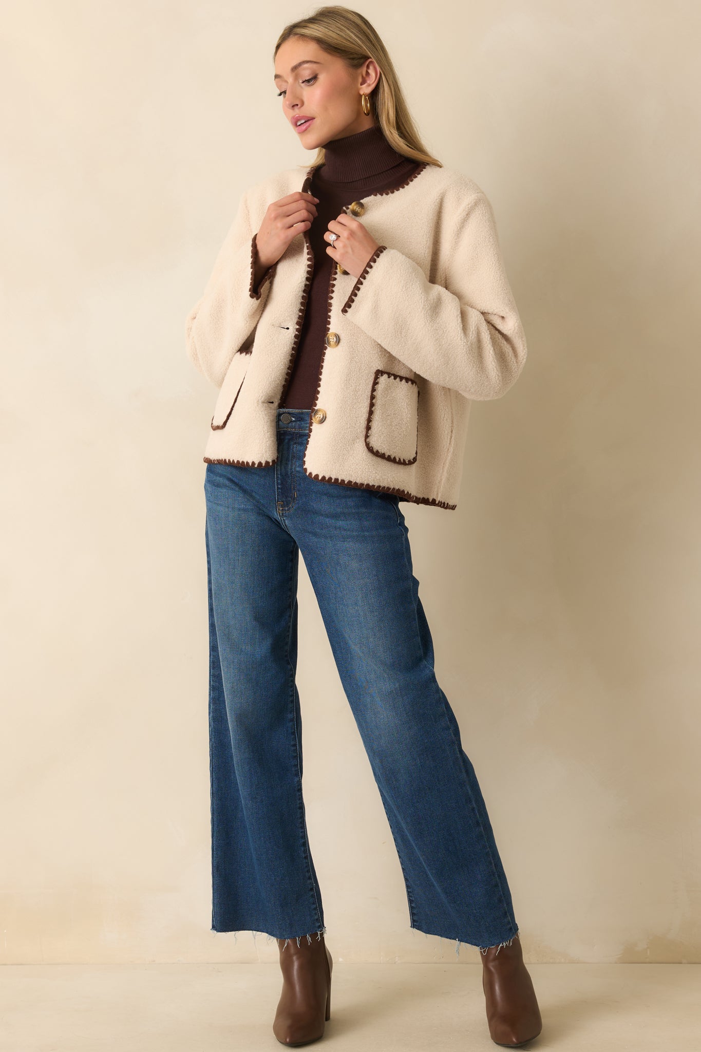 Cozy fleece jacket in ivory featuring long sleeves, patch pockets, and contrasting brown stitching along the edges.