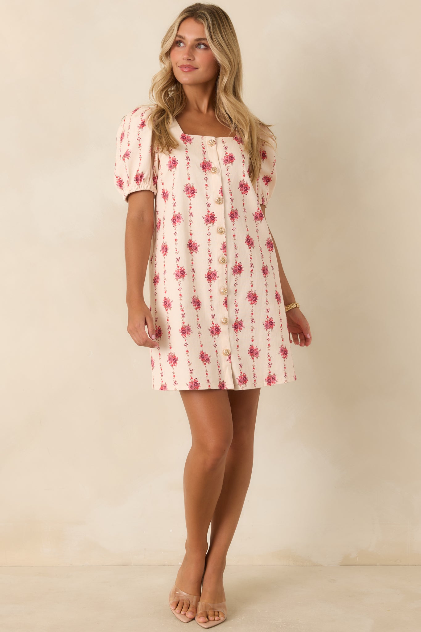 Ivory floral mini dress featuring rose bouquet prints, trailing vines, square neckline, puff sleeves, gold-tone buttons, and hidden pockets.