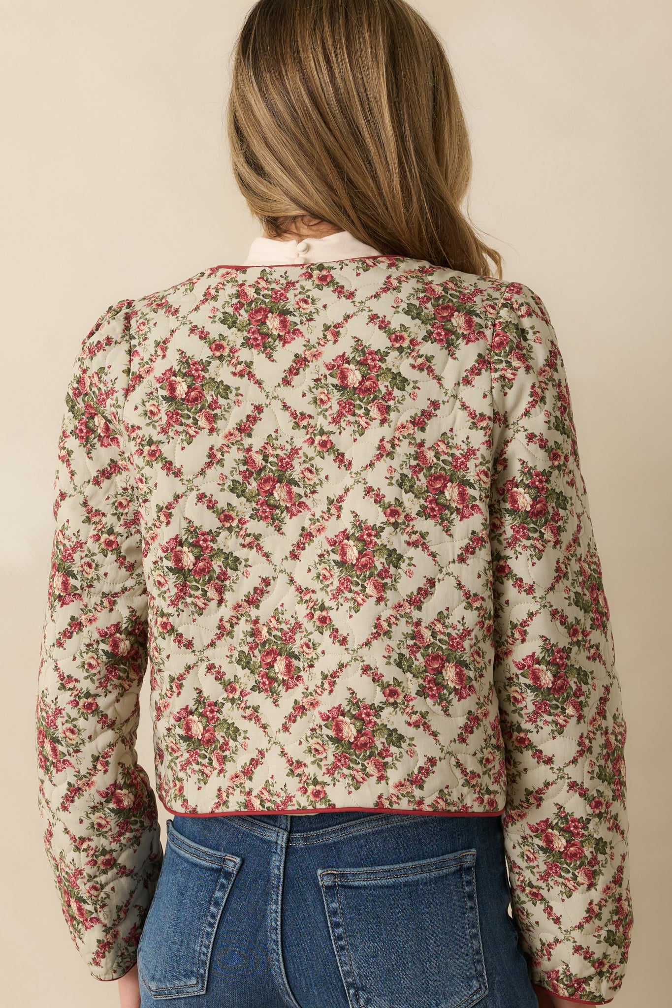 Rear view of ivory floral quilted jacket featuring red trim and smooth, lightly padded finish.
