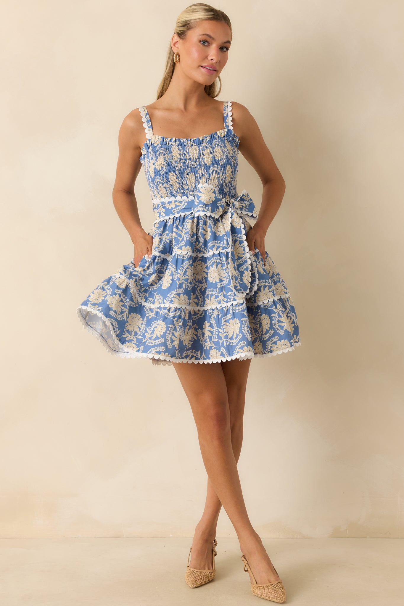 Ivory and dusty blue floral dress featuring scalloped trim accents, a defined waist sash, and a feminine fit-and-flare shape.