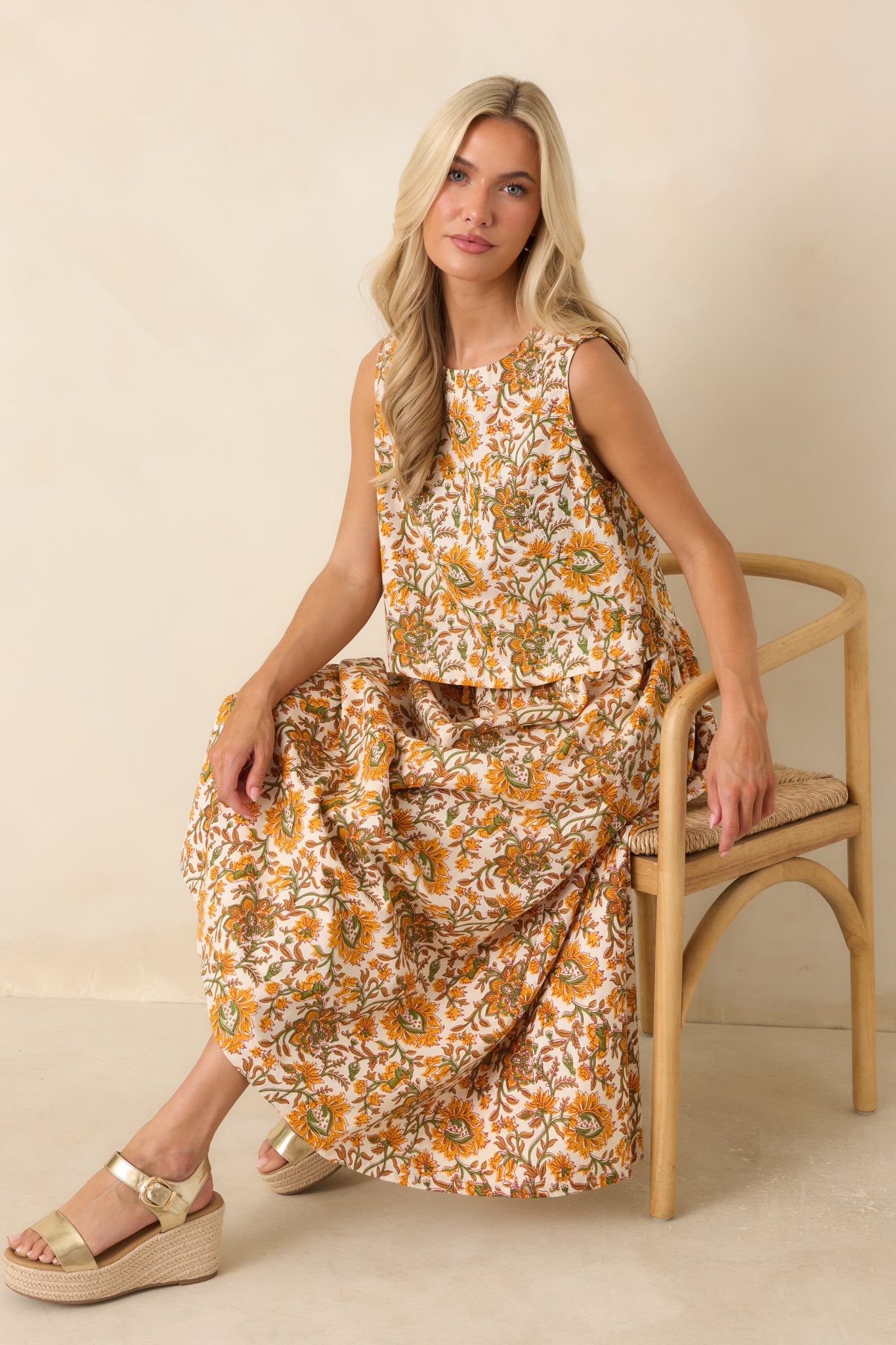 Full-length view of a sleeveless cropped top featuring an ivory background with marigold, olive, and tan floral detailing and a high neckline.
