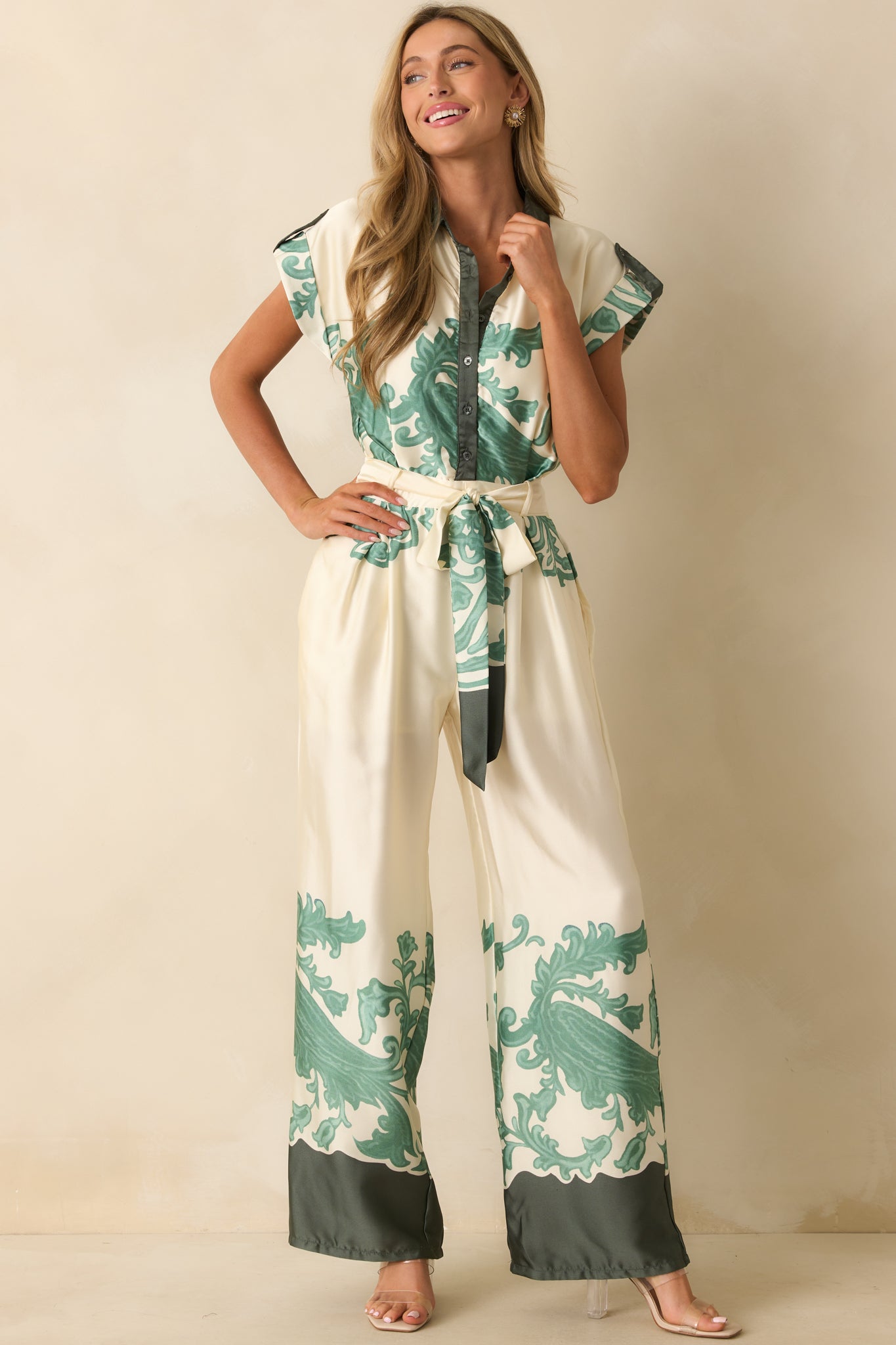 Ivory jumpsuit with optional sash tied at waist, emphasizing wide-leg fit and ornate green border print.