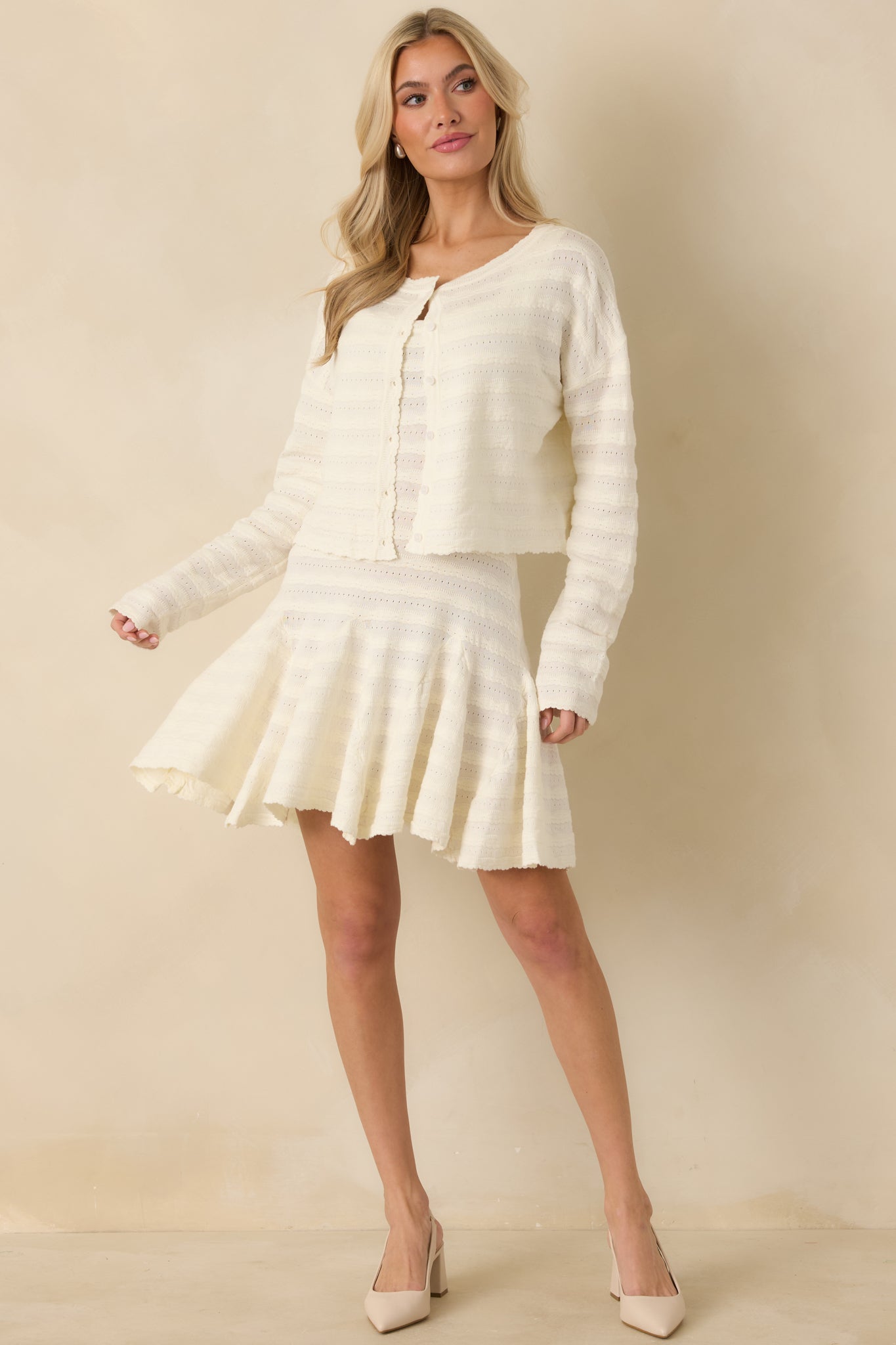 Ivory knit cardigan with a delicate textured finish, full button-front closure, and gently scalloped neckline flowing into a matching hem.
