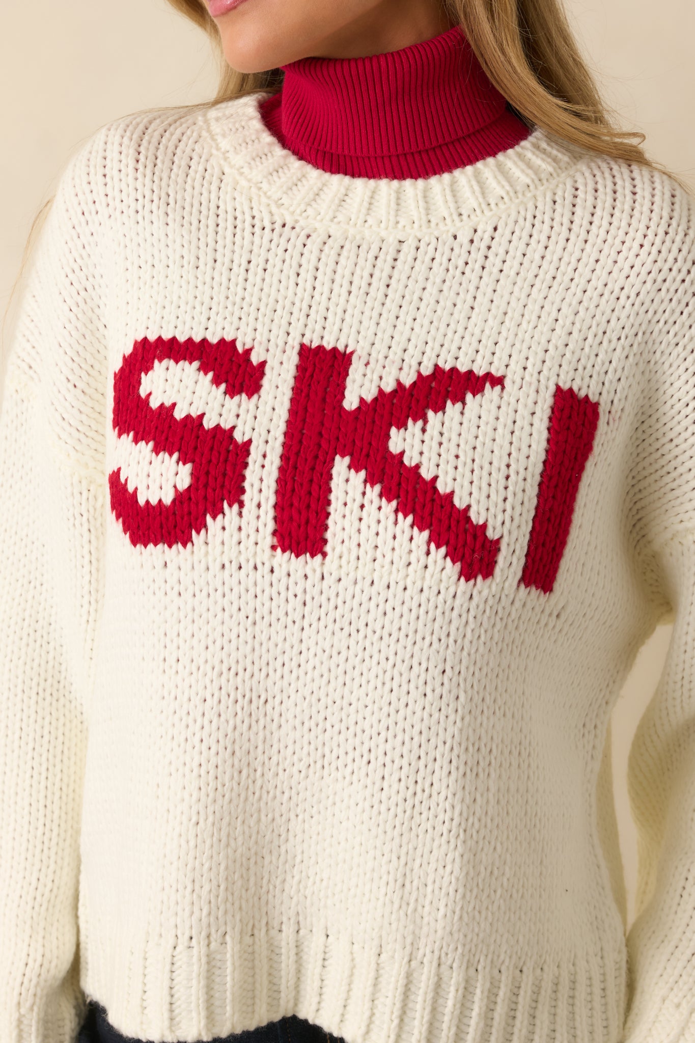 Close-up of ivory knit texture with ribbing and red “SKI” lettering detail.